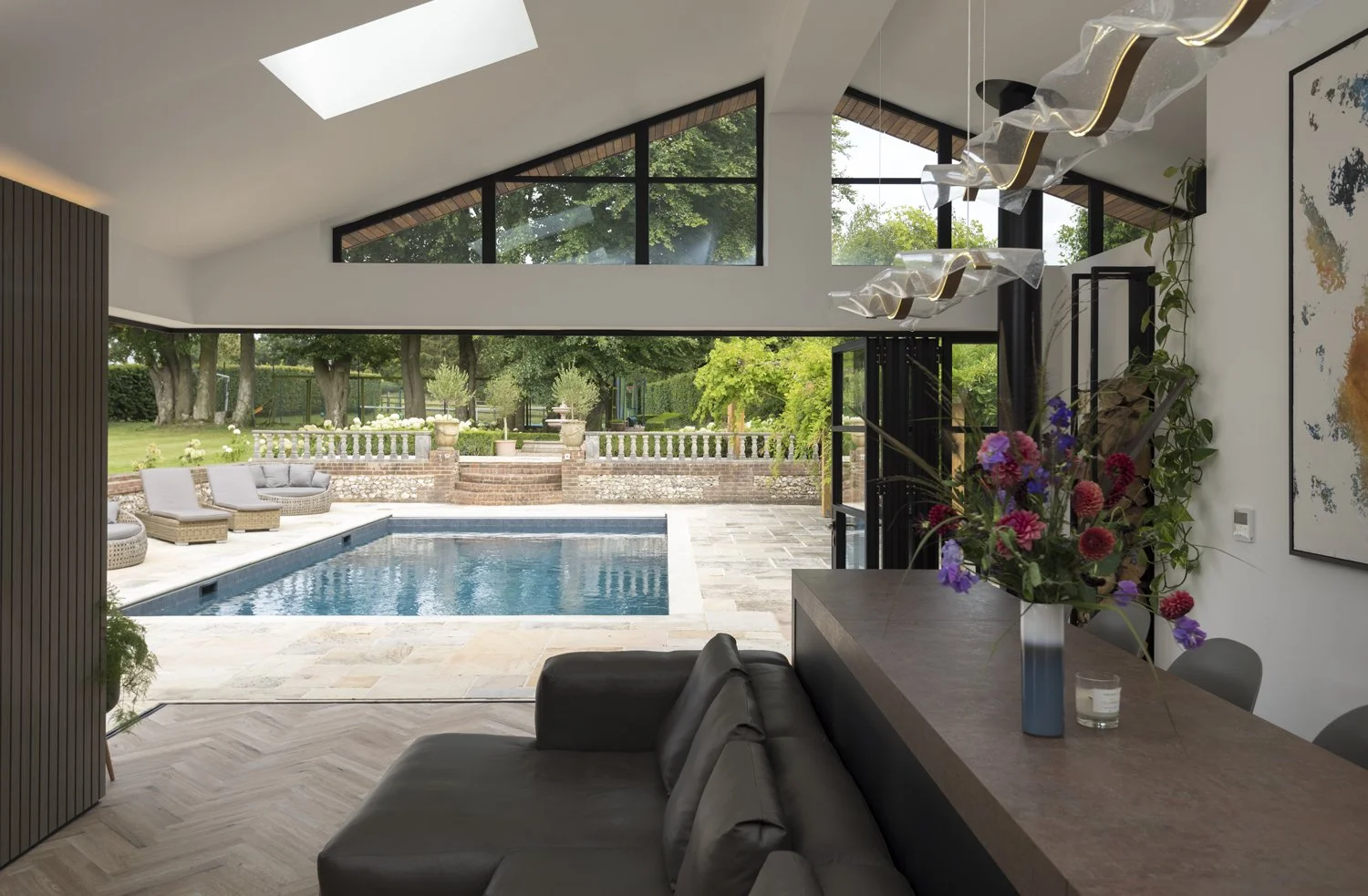Modern living room with large windows overlooking a backyard with a swimming pool and garden, featuring lounge chairs and decorative pots.