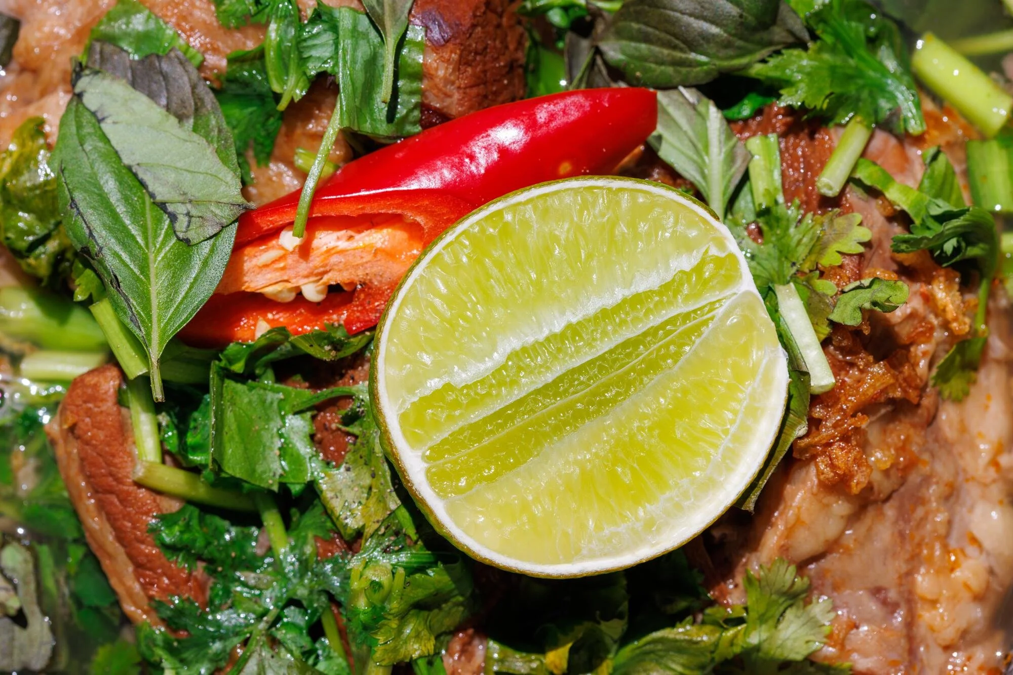 Gedeckter Teller mit Limettenscheiben, rotem Chili, frischen grünen Kräutern und Fleisch.
