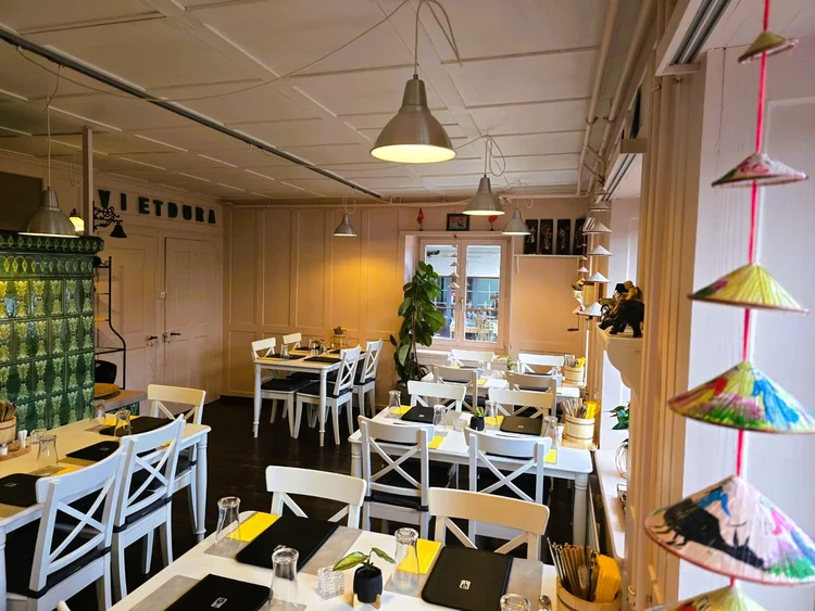 Gastraum vom Restaurant Vietdura mit weissen Tischen, Pflanzen, vietnamesischen Hüten und Fenstern.