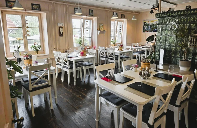 Grüner Kachelofen im Restaurant Vietdura Tagelswangen ZH, davor ein langer gedeckter Tisch mit vietnamesischem Reishut und Zimmerpflanzen.