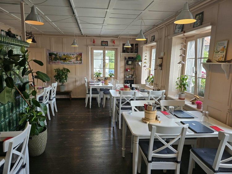 Blick in den Gastraum vom Restaurant Vietdura in Tagelswangen ZH: weisse Tische und Stühle, Fenster zur Zürcherstrasse und der grüne Kachelofen im Hintergrund.