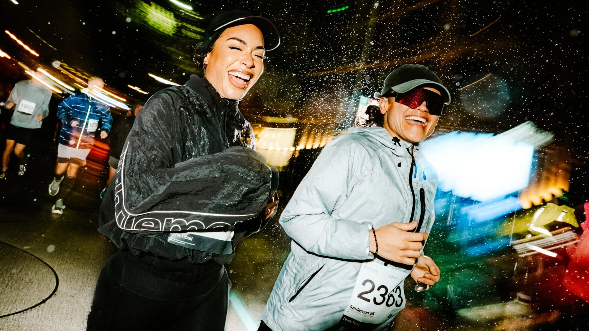 Two smiling people run side-by-side outside at night.