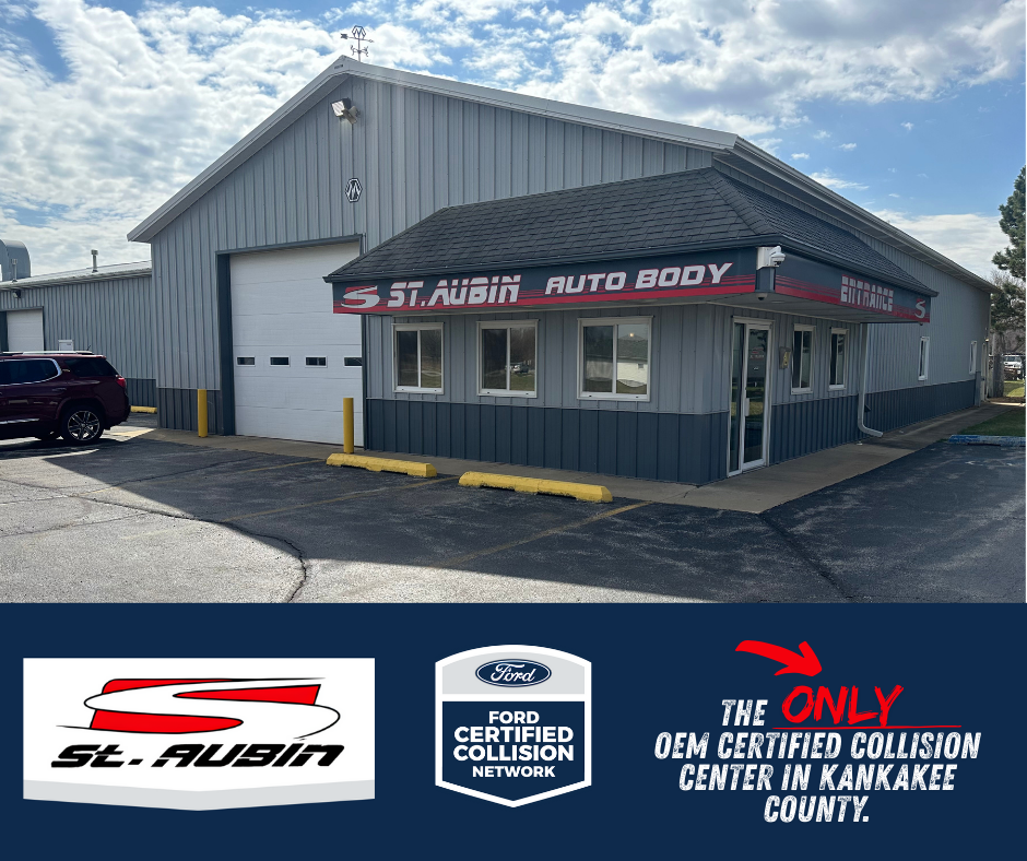 Exterior of St. Aubin Auto Body shop with a gray metal building, a large garage door, and a small office entrance with windows, parking lot with a few cars, and a sign displaying business details.