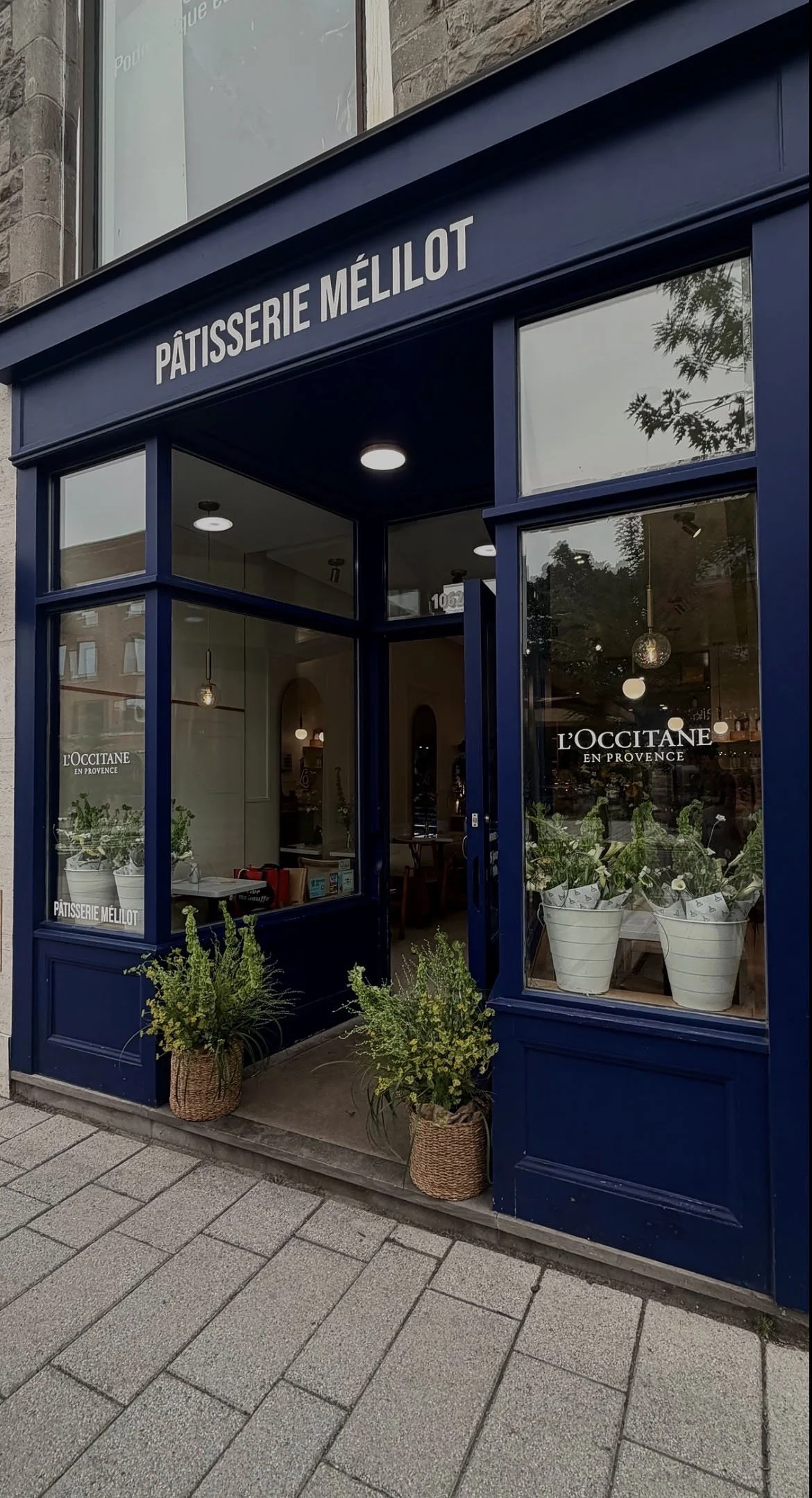 Façade d'une pâtisserie nommée 'Pâtisserie Méliott' avec une devanture en bleu foncé, fenêtres laissant entrevoir l'intérieur, et des plantes en pot à l'extérieur.
