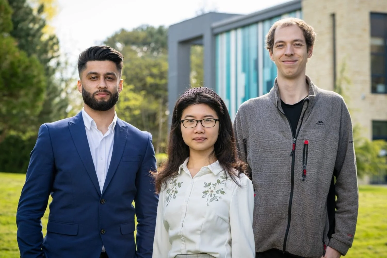 Three young professionals outdoors, standing in front of a modern building, smiling at the camera.