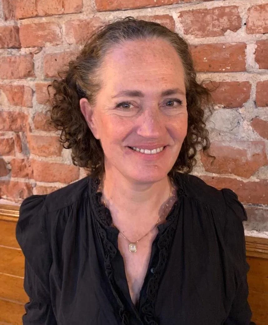 Sarah Turner, Angel Academe co-founder with short curly hair wearing a white shirt with a ruched collar, photographed in profile view.