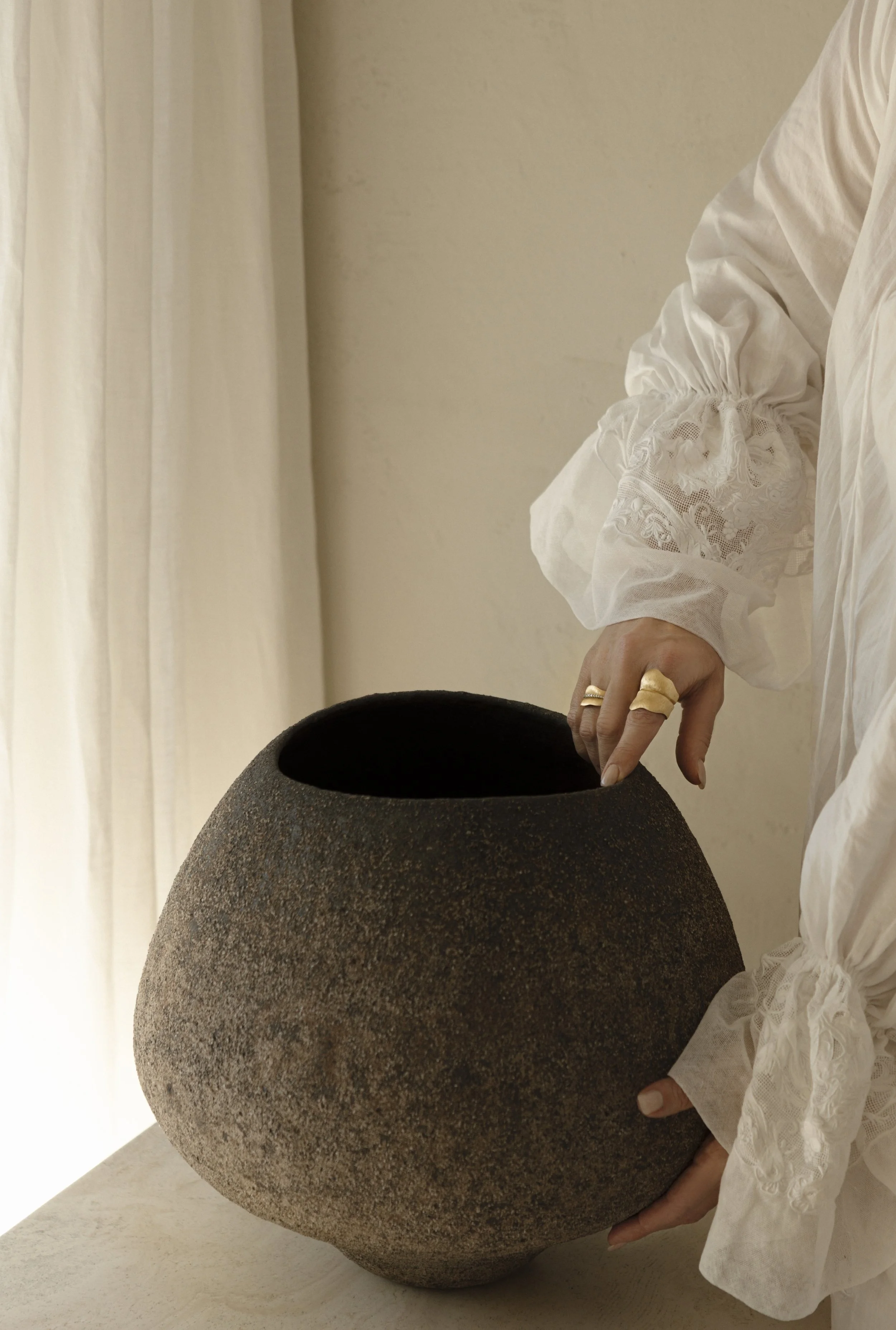 valeria-viollaz-holding-hiroshi-aoki-ceramic-vessel-travertine-pedestal-linen-dress-gold-rings-vv-interior-home-lucerne-switzerland-perspectives.jpg