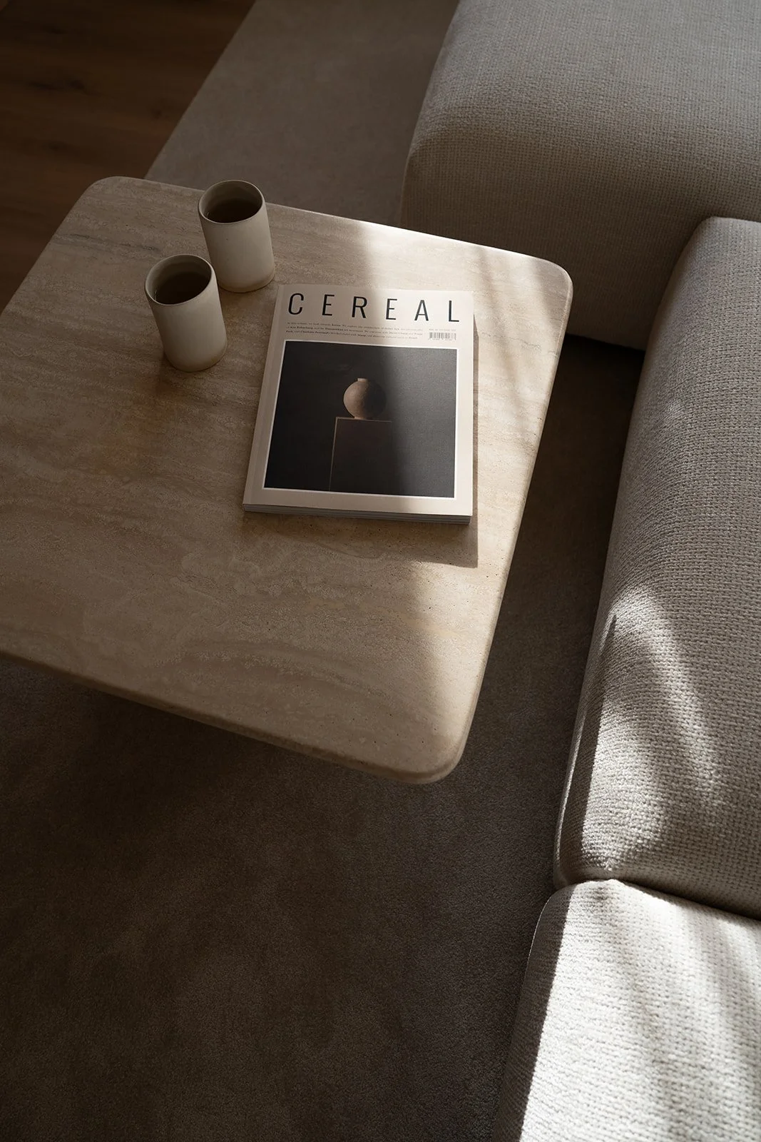 Travertine coffee table with ceramic cups beside neutral upholstered seating, a Riccardo Rossi project with curation by Valeria Viollaz for VV Interior Home. Photo: Cornelia Kindsvater.