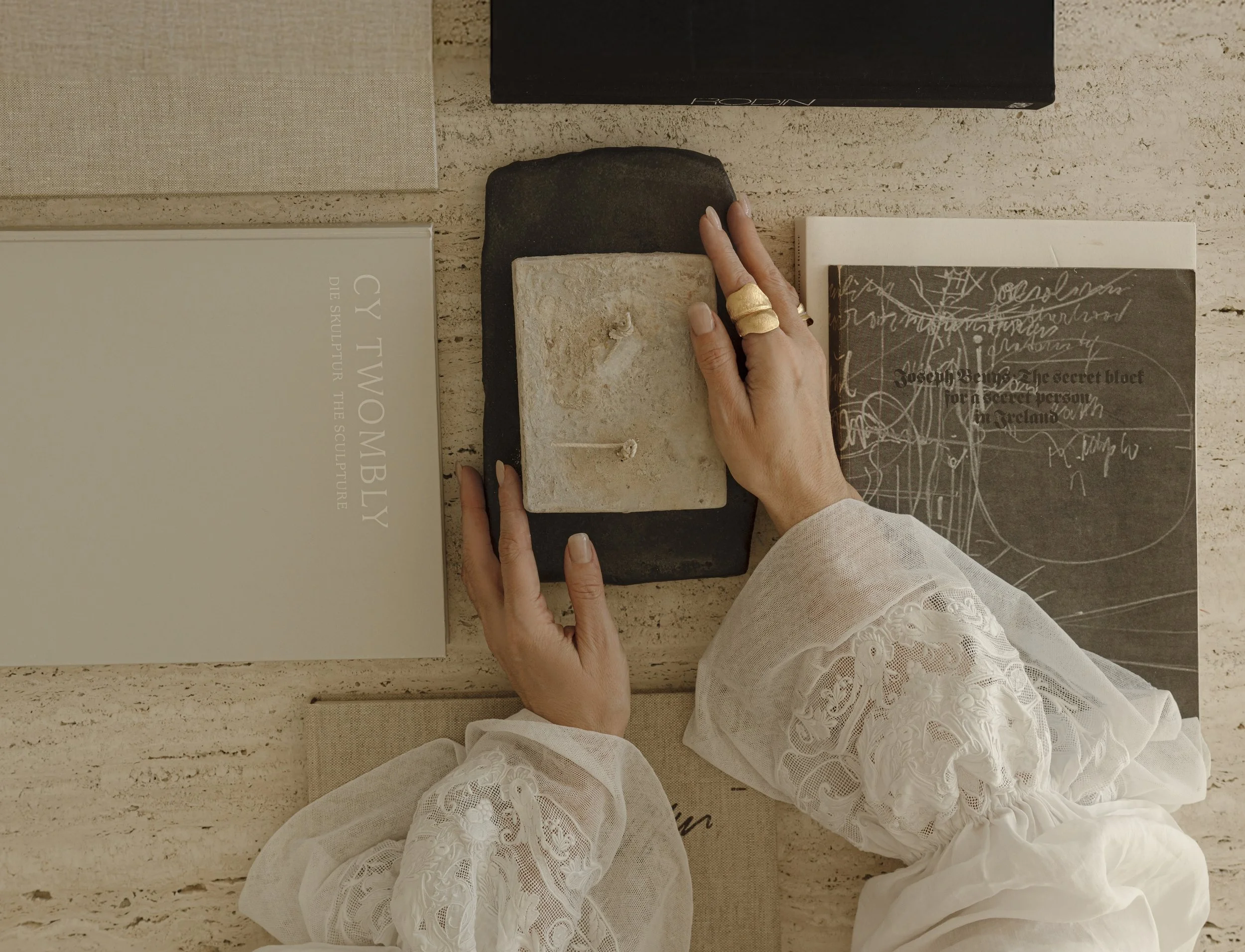Overhead view of a curated tabletop featuring a Cy Twombly art book, gold Ole Lynggaard Copenhagen jewelry, and artisanal stone objects.