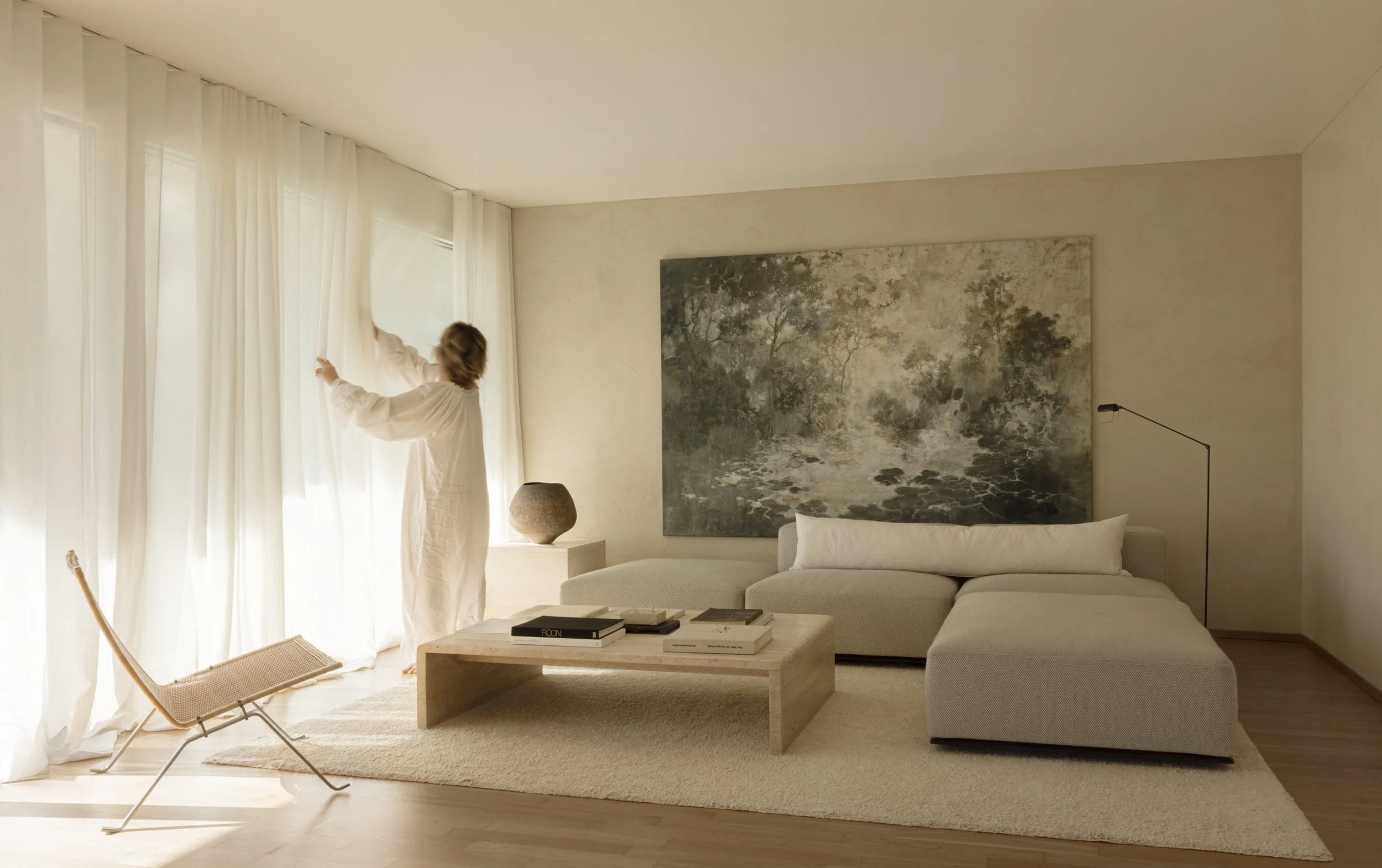 A minimalist living room curated by Valeria Viollaz featuring a large Hiroshi Aoki landscape painting, textured walls by Pure Original Paint, and a low travertine coffee table.