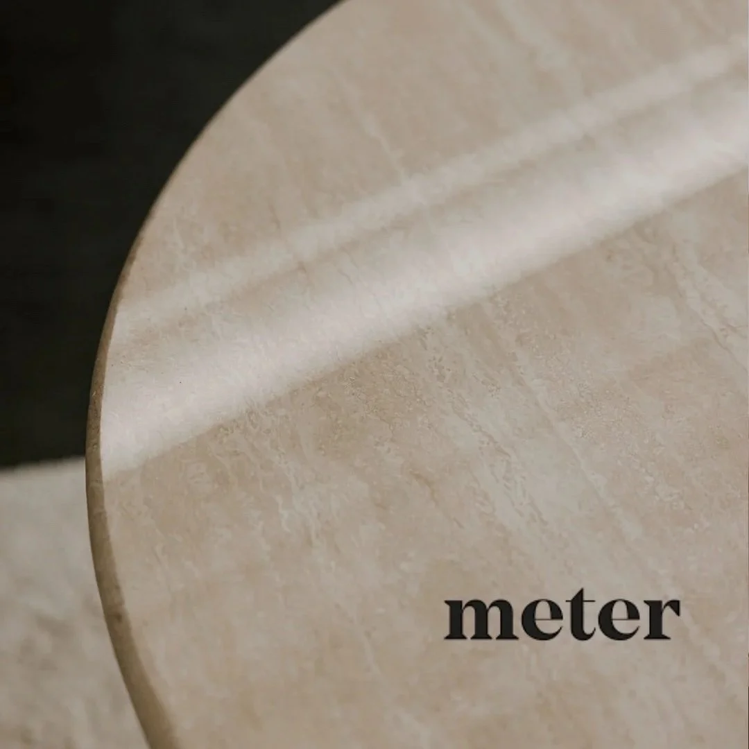 Close-up of a beige marble round table with the word "meter" printed in black.