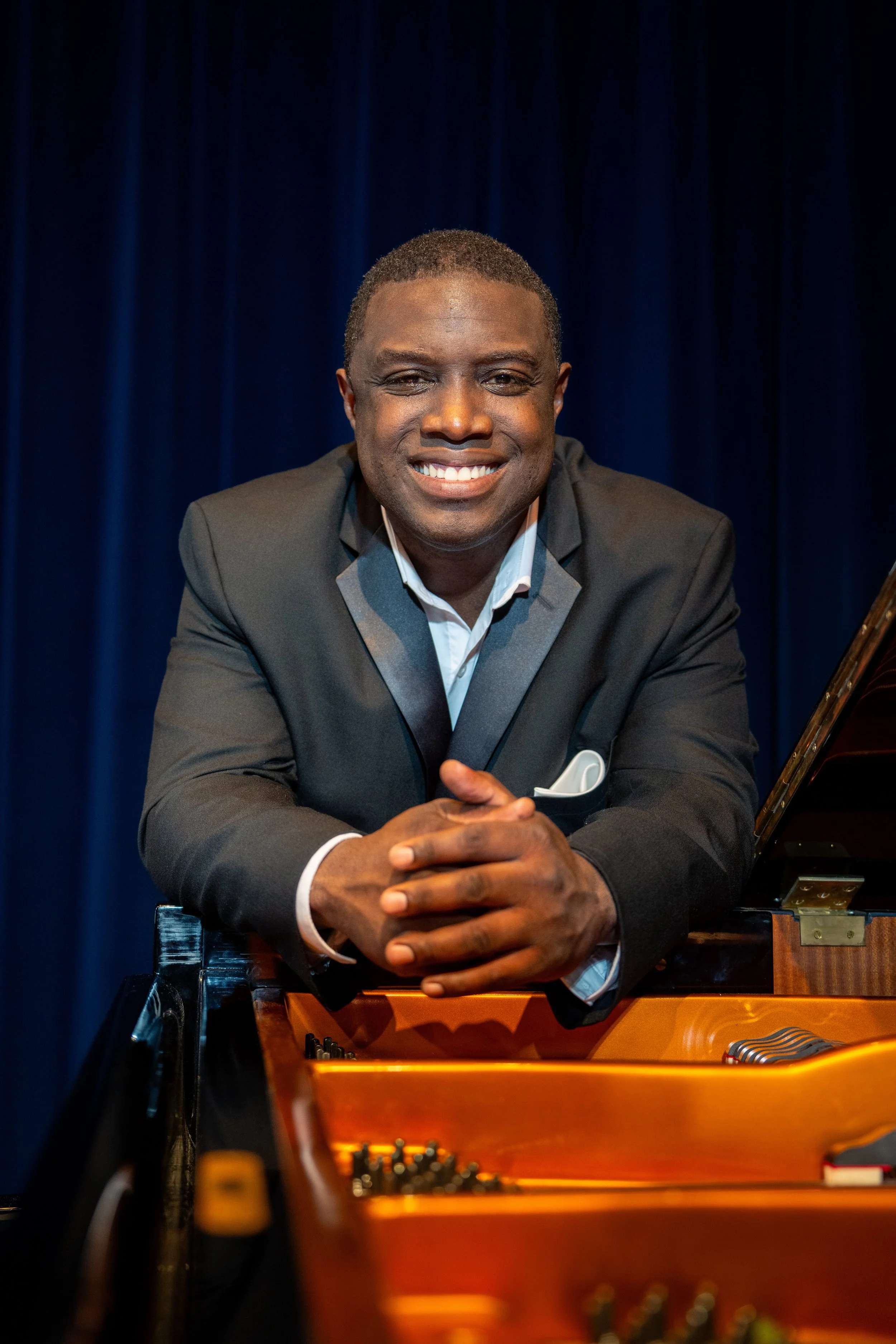 A smiling man with short black hair wearing a black blazer