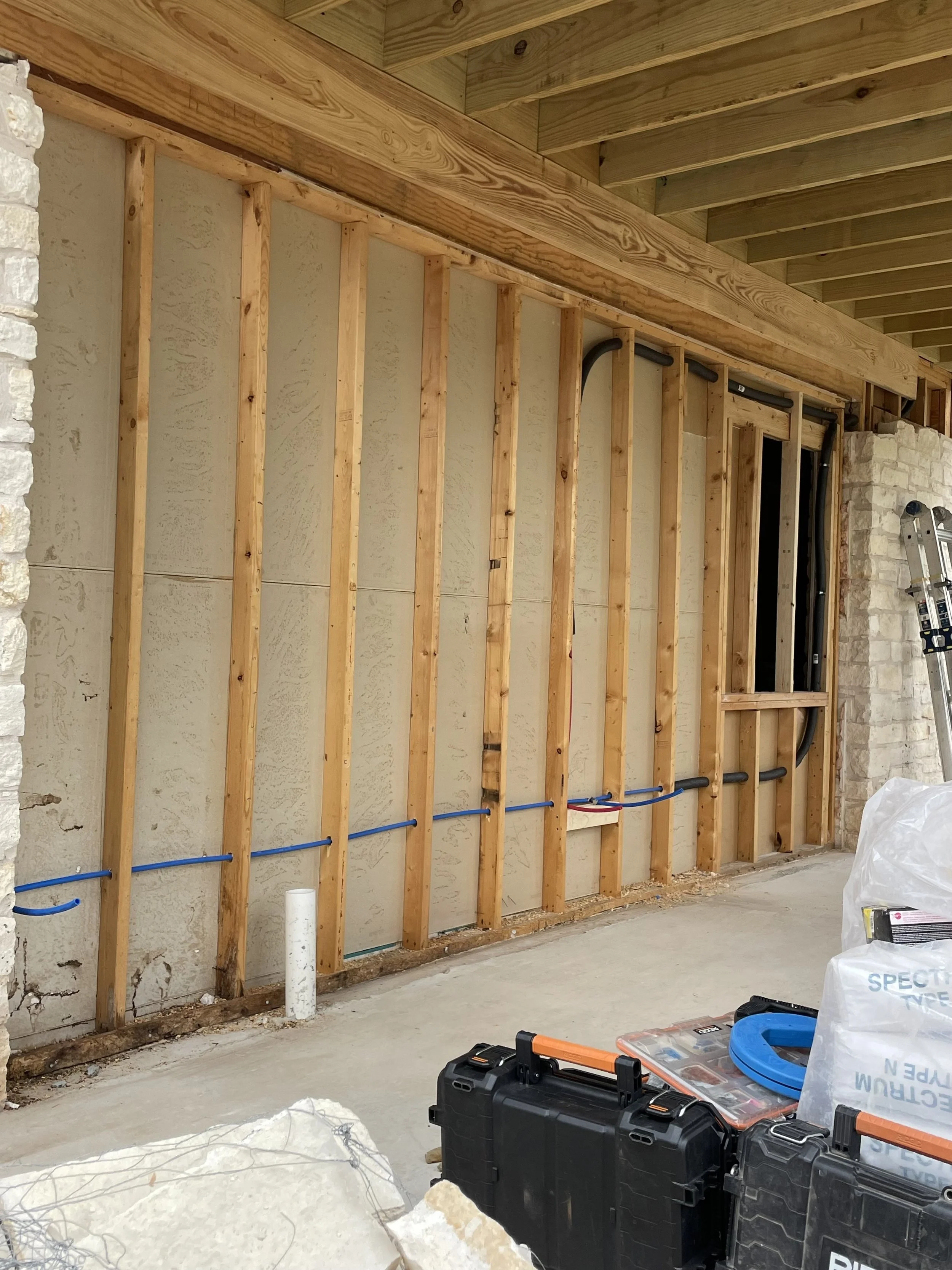 Interior view of a construction site with exposed wooden wall framing, electrical conduit, and construction tools.