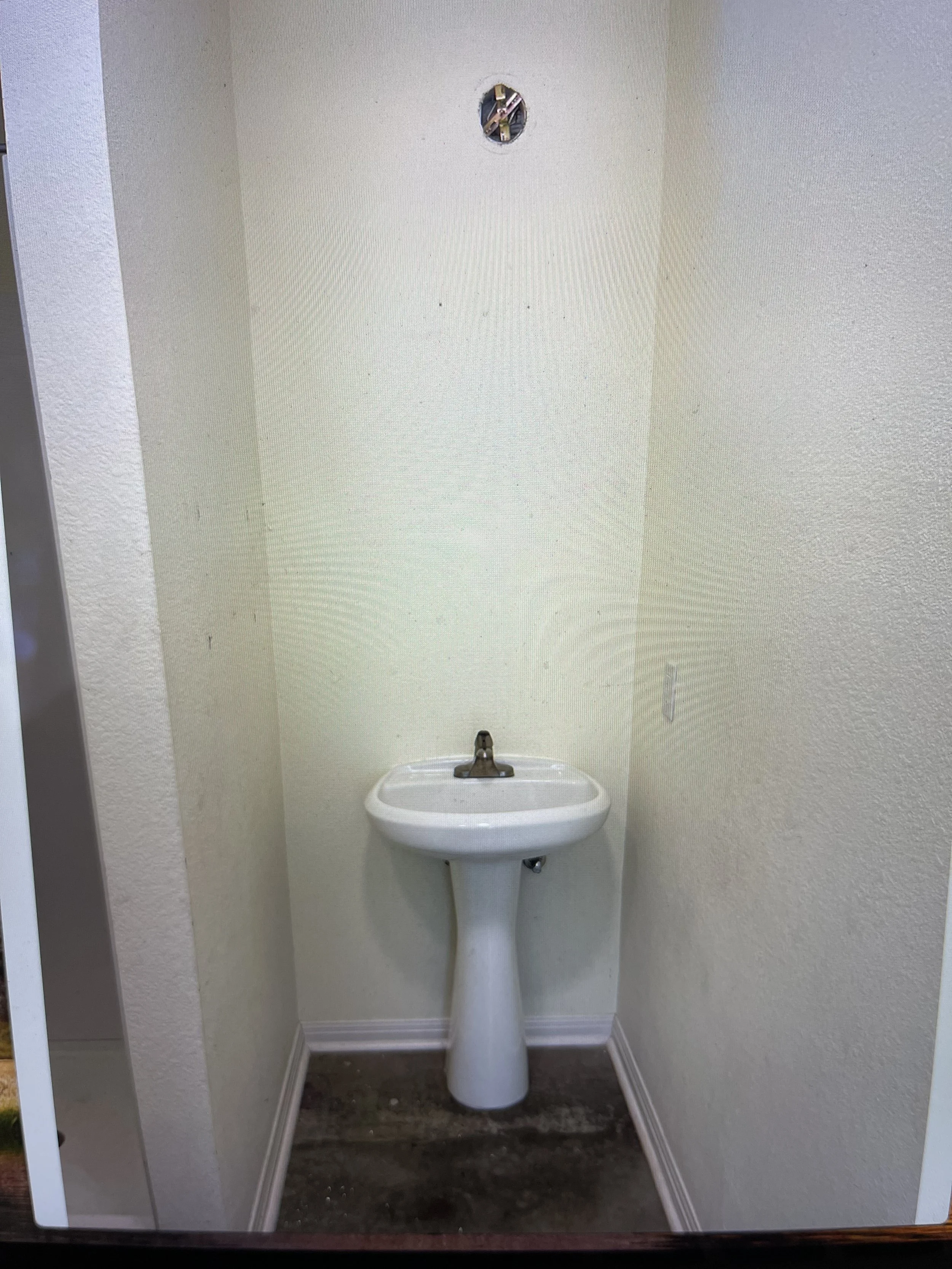 A small white wall-mounted sink with a faucet, set against a beige textured wall with a hole near the top.