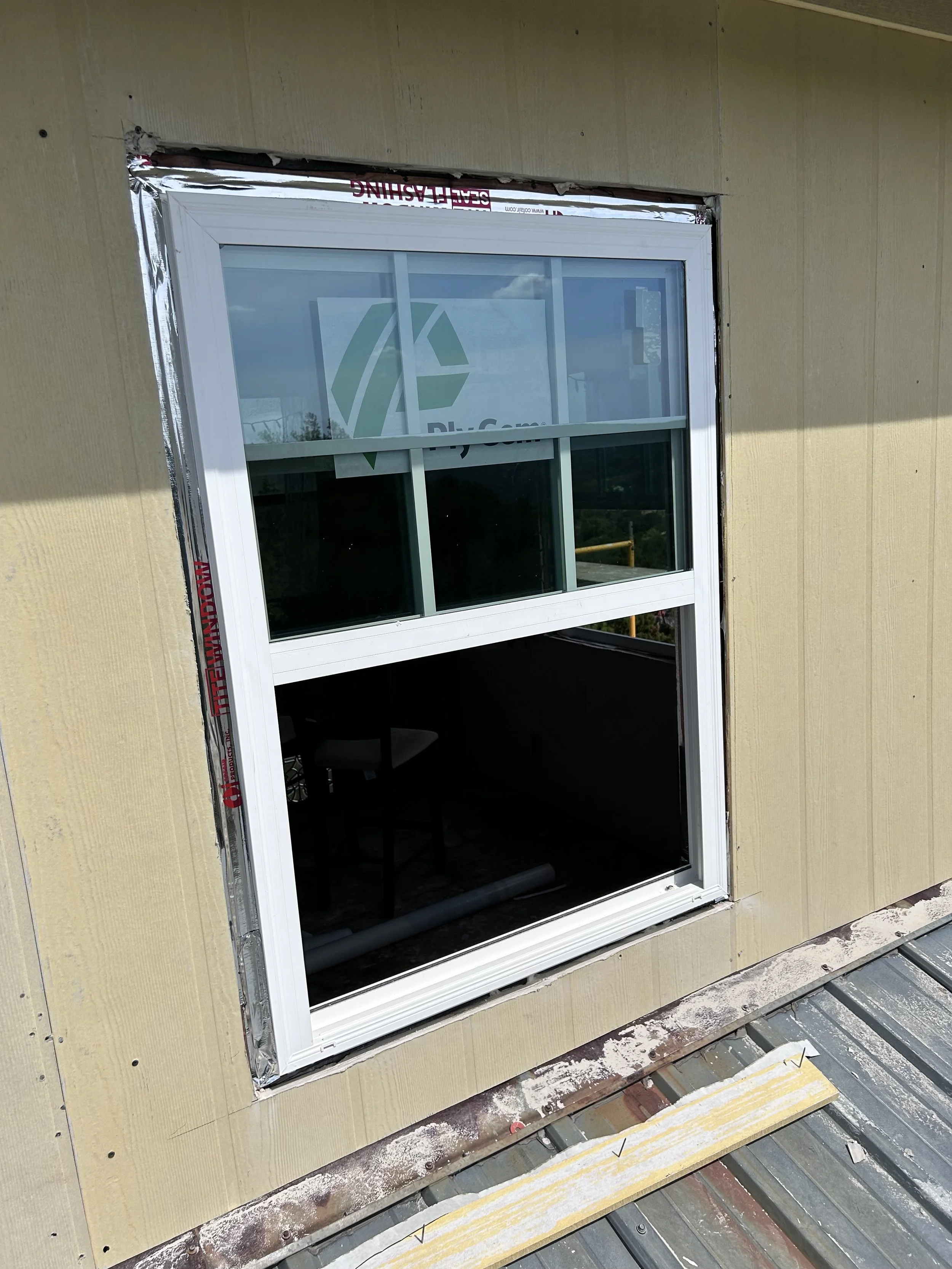 New double-hung window installed on the exterior of a building under construction, with insulation and unfinished siding around it.