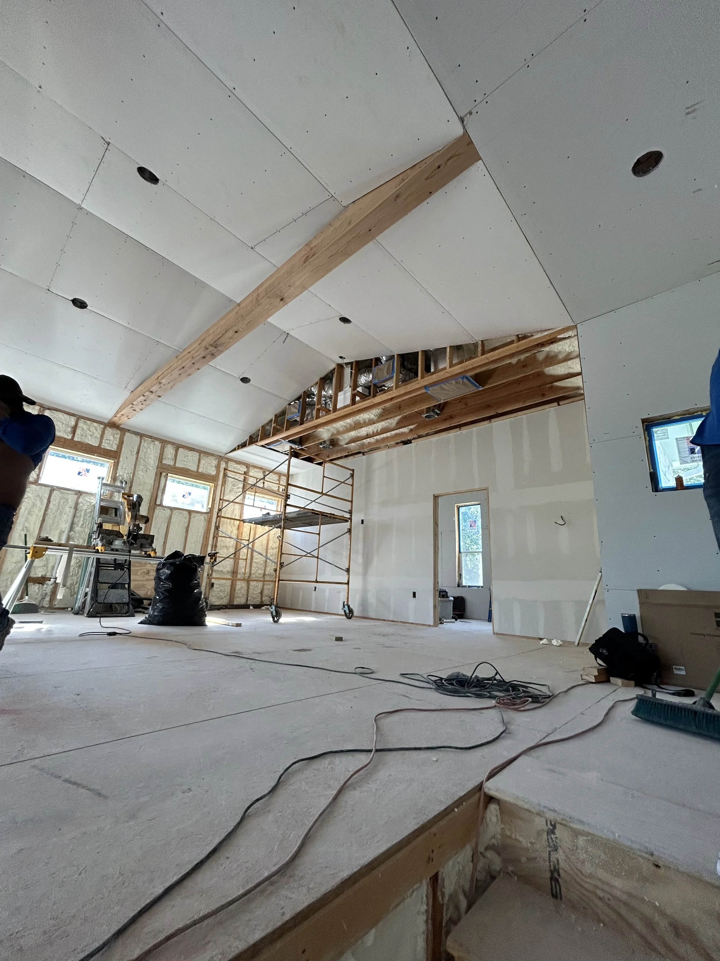 Interior view of a house under construction with scaffolding, drywall, and construction tools, showing an arched ceiling with wood beams.