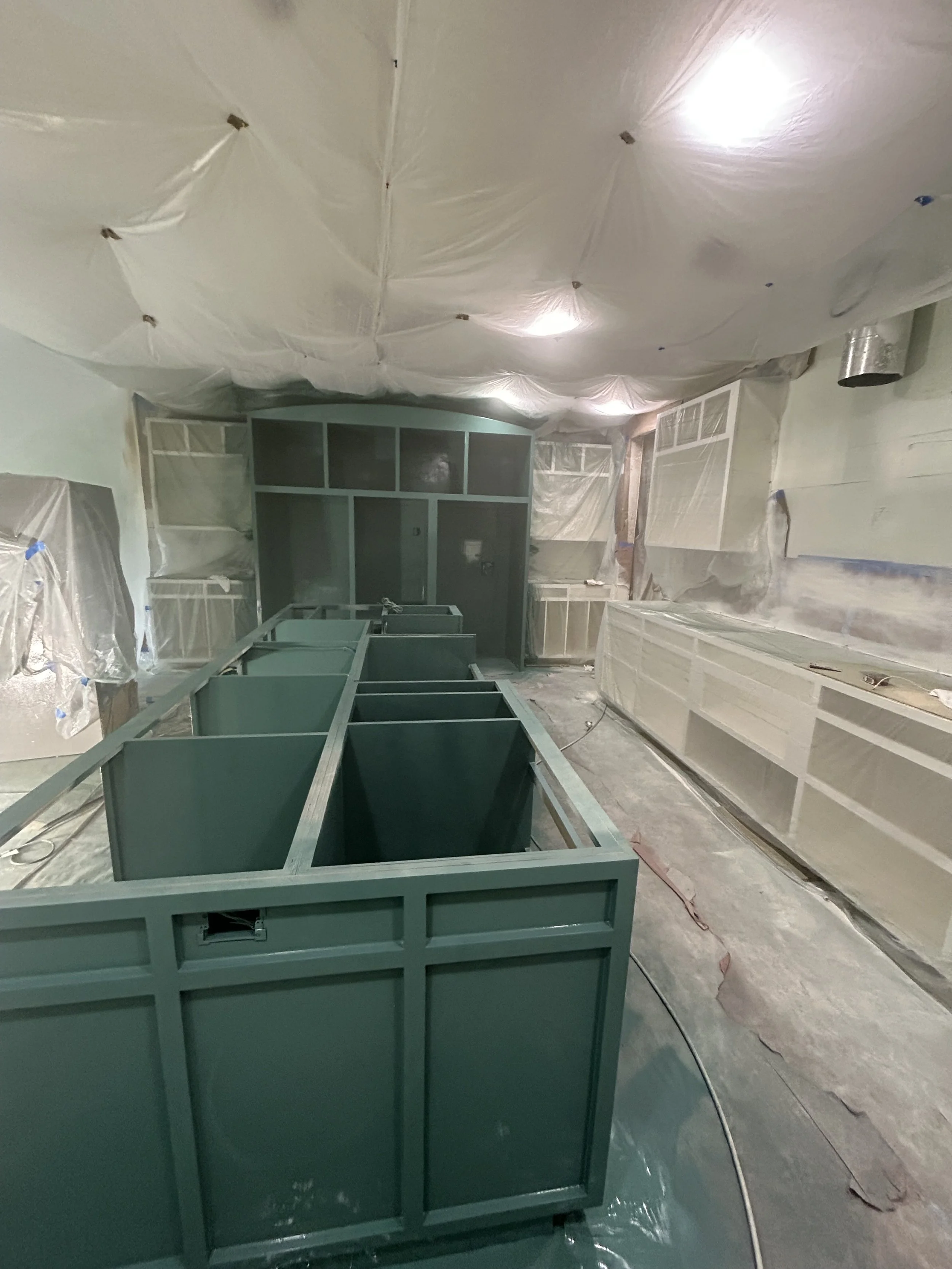Construction site with partially assembled green cabinets and unfinished walls covered in plastic sheeting.