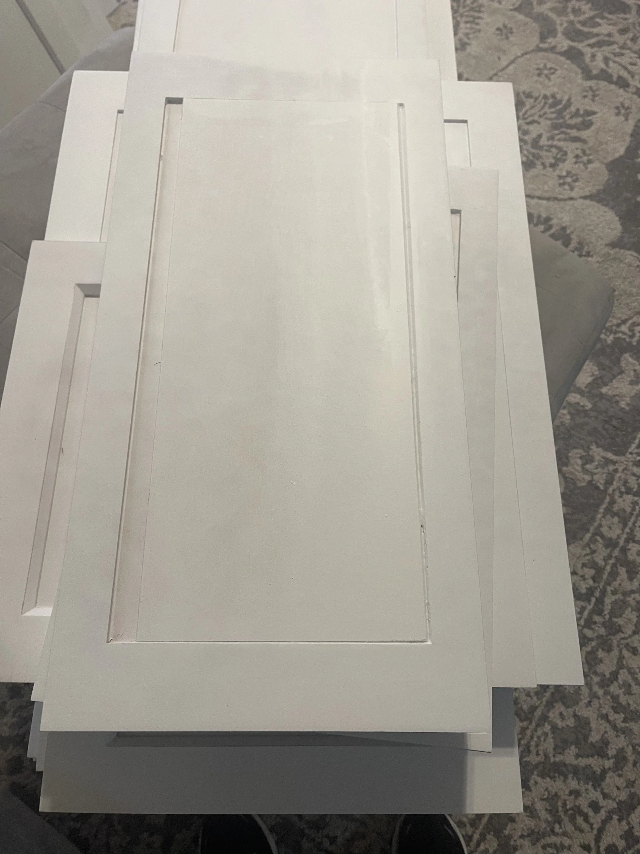 Stacked white cabinet or door panels on a table with a patterned rug in the background.