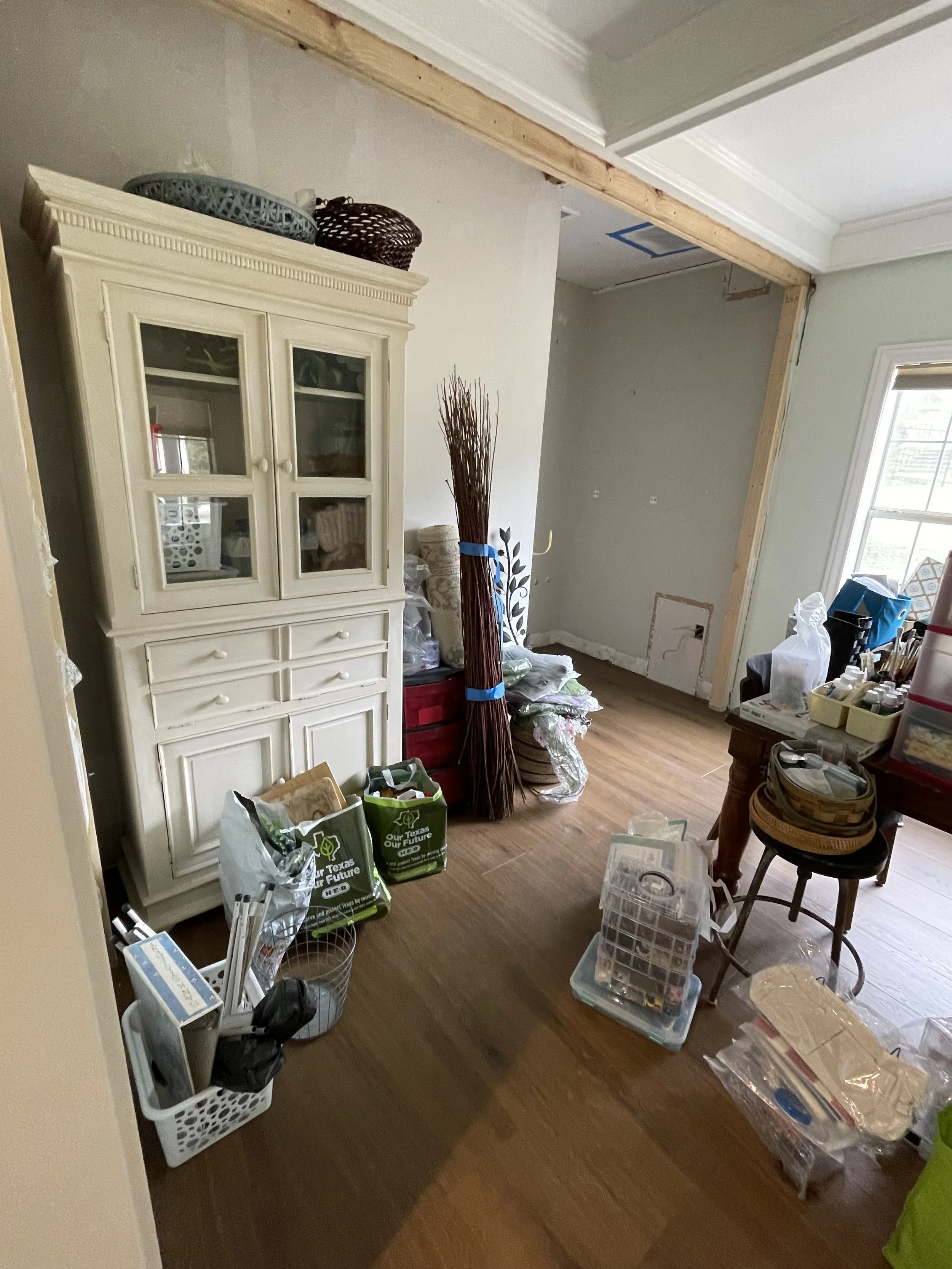 Room under renovation with various household items, a white cabinet, broomstick, storage bins, and construction materials.