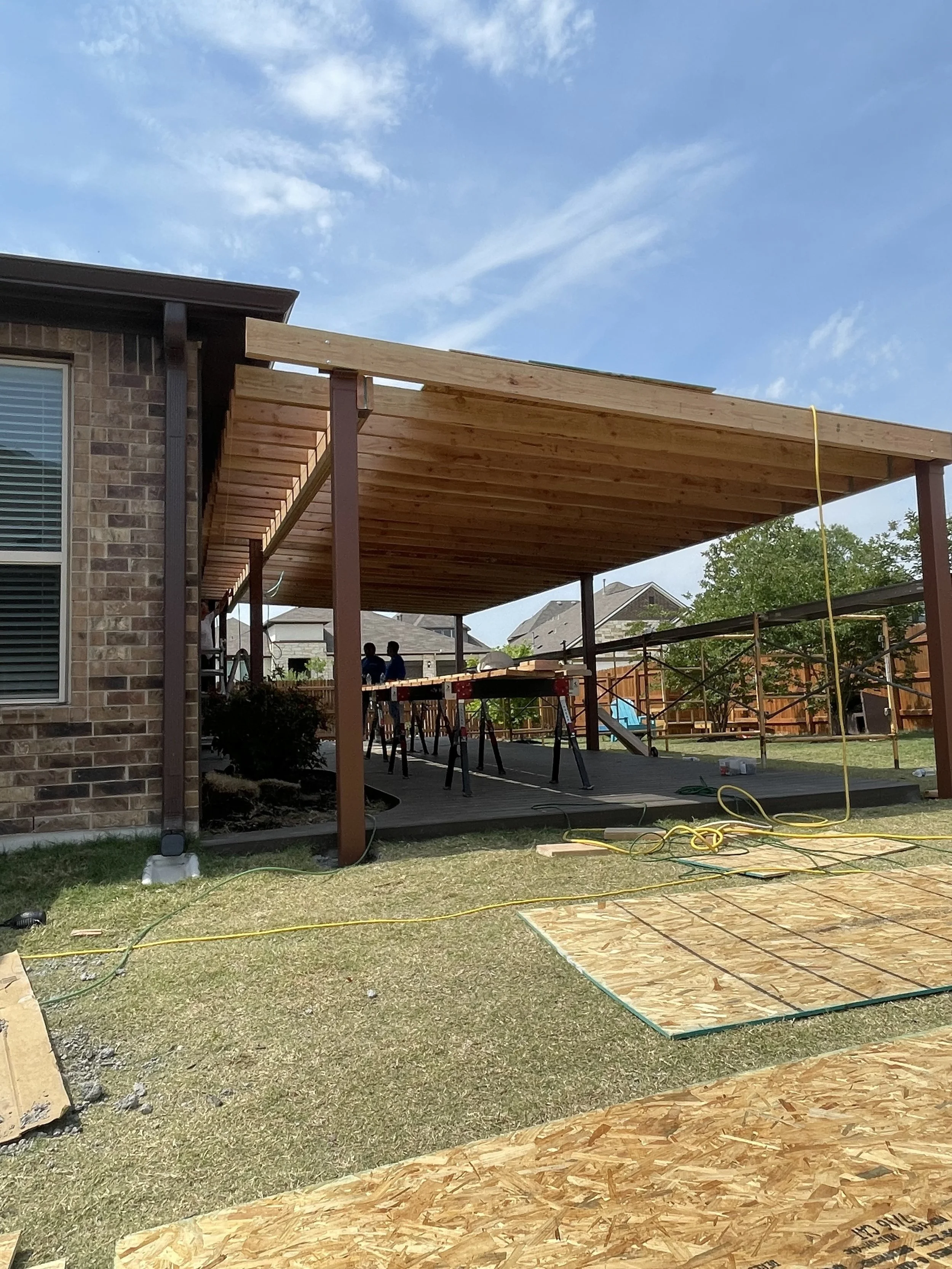 Construction of a wooden porch extension on a brick house, with scaffolding and construction tools present.