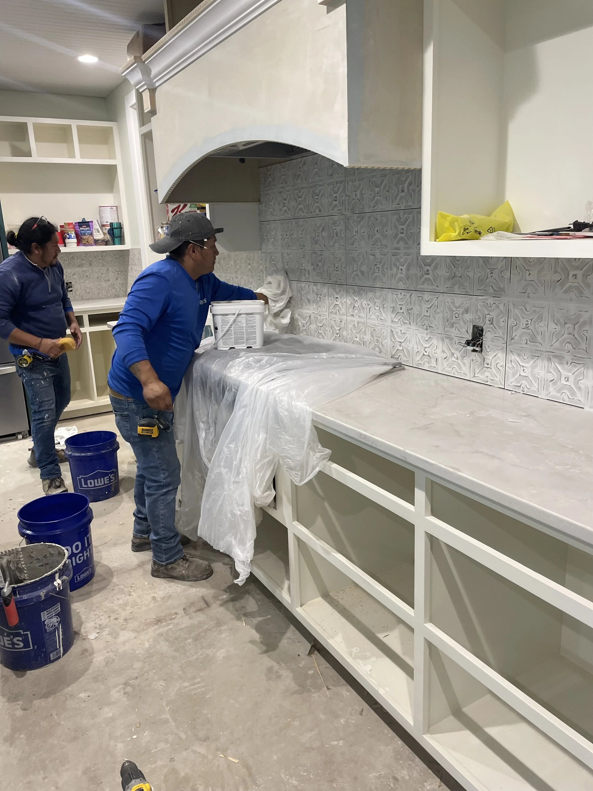 Two people working on a kitchen renovation, applying a new countertop, with tools and supplies around them.