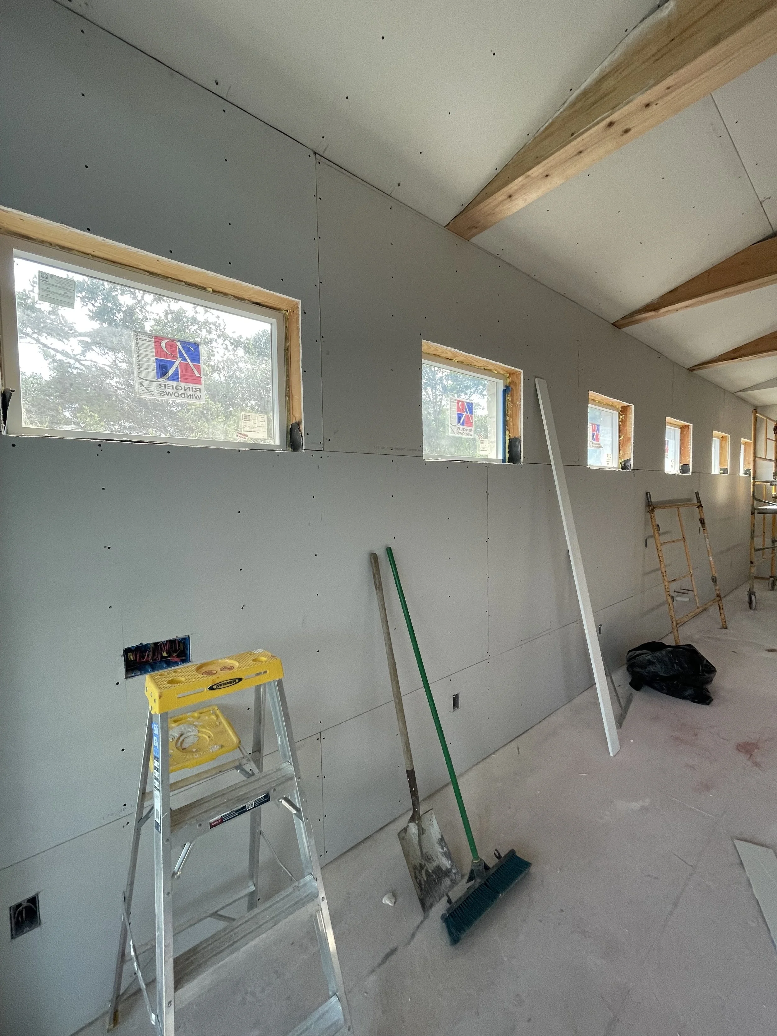 Interior wall under construction with small windows, tools, and scaffolding.