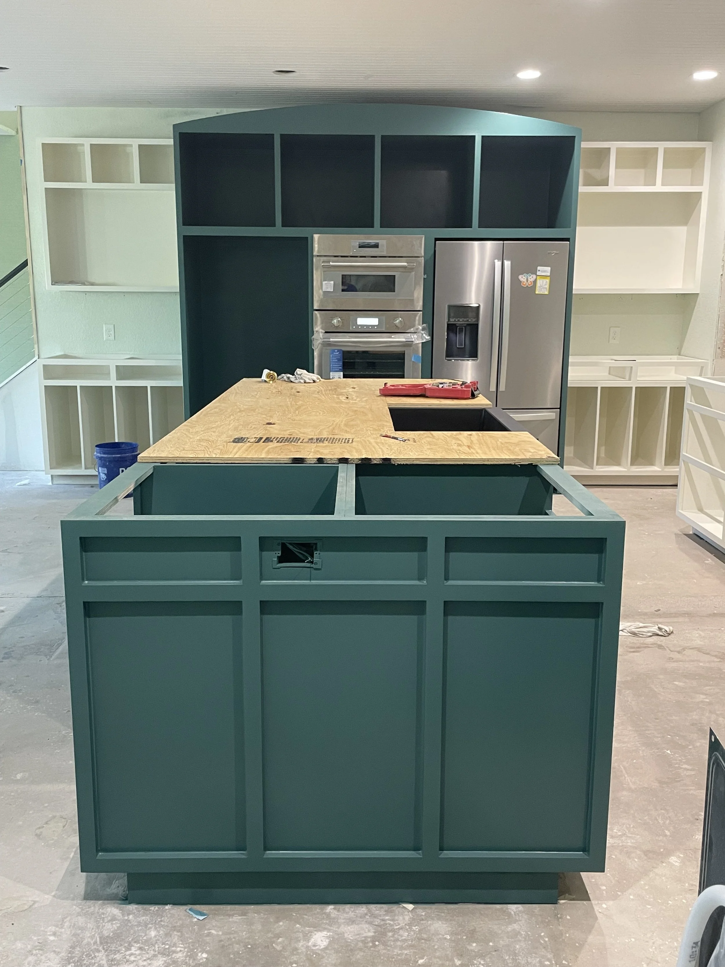 Kitchen island with wooden countertop and green painted cabinetry in a kitchen under construction.