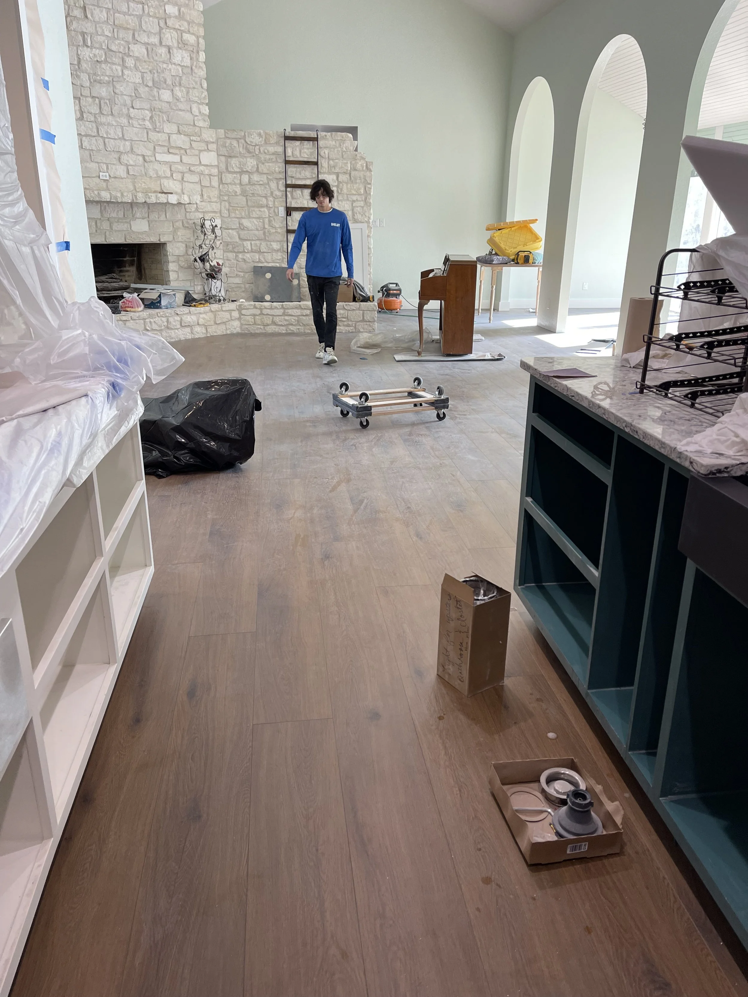 Interior of a house under renovation with a person walking across the room, construction tools and materials scattered around.