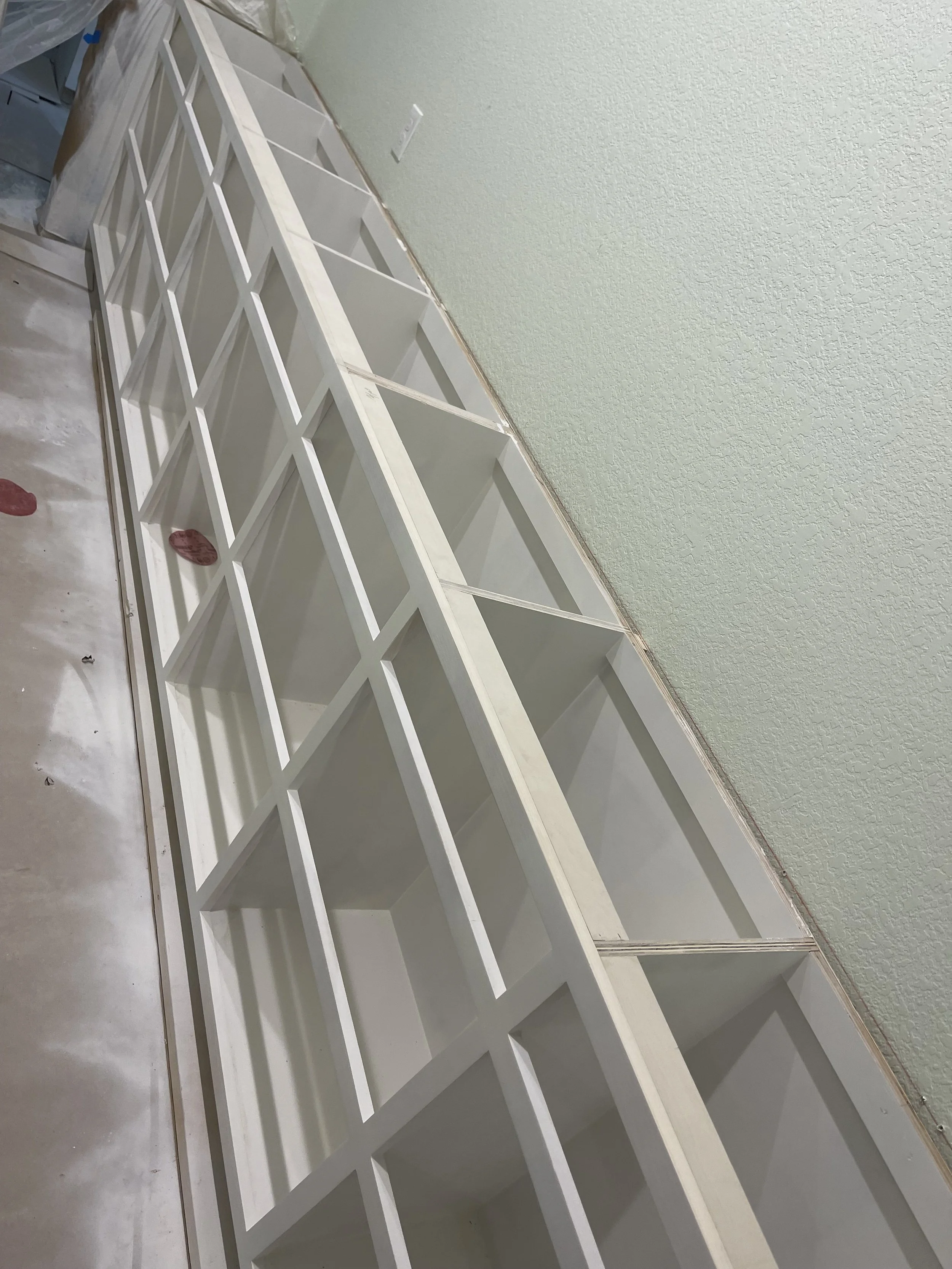 White wooden shelving unit with multiple compartments positioned against a green textured wall in a room under construction or renovation.