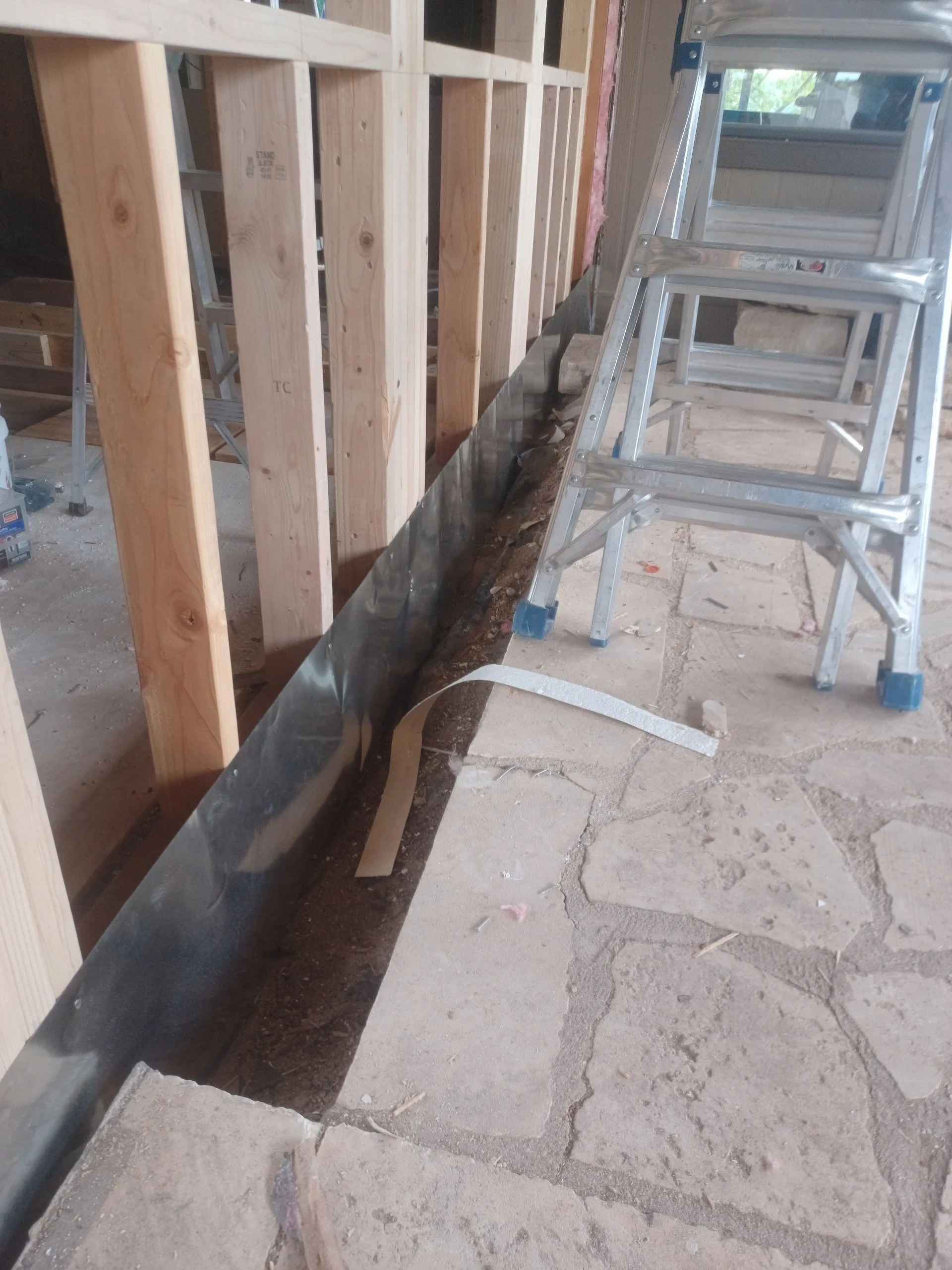 Construction site with wooden framing, a metal piece, and a step ladder on a stone floor.