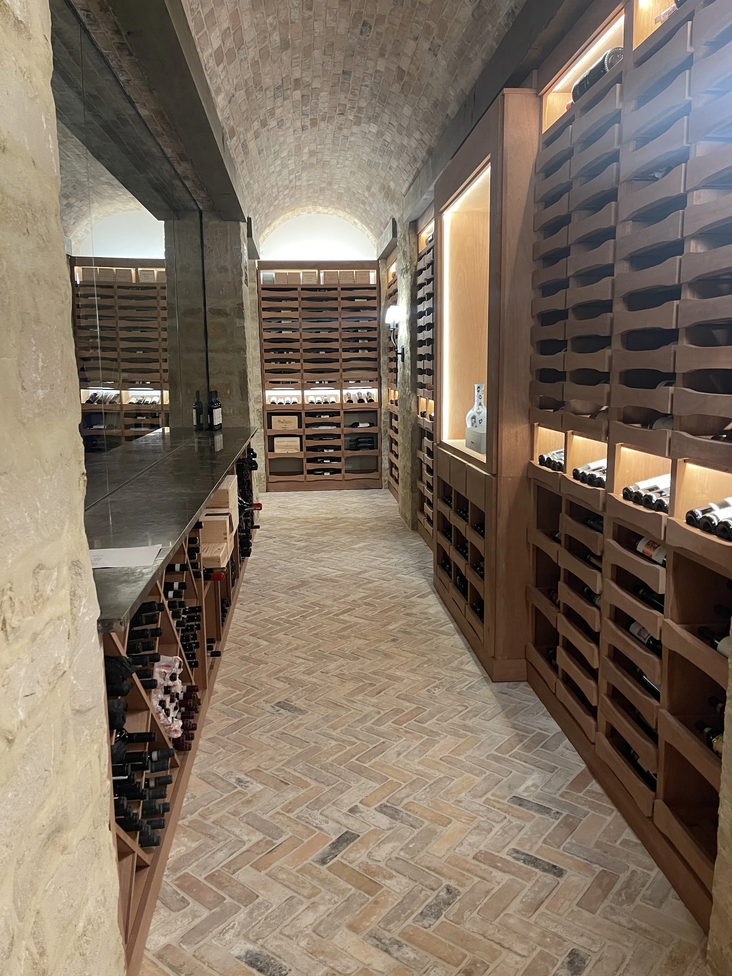 Wine cellar with arched stone ceilings, wooden racks of wine bottles, and illuminated display shelves.