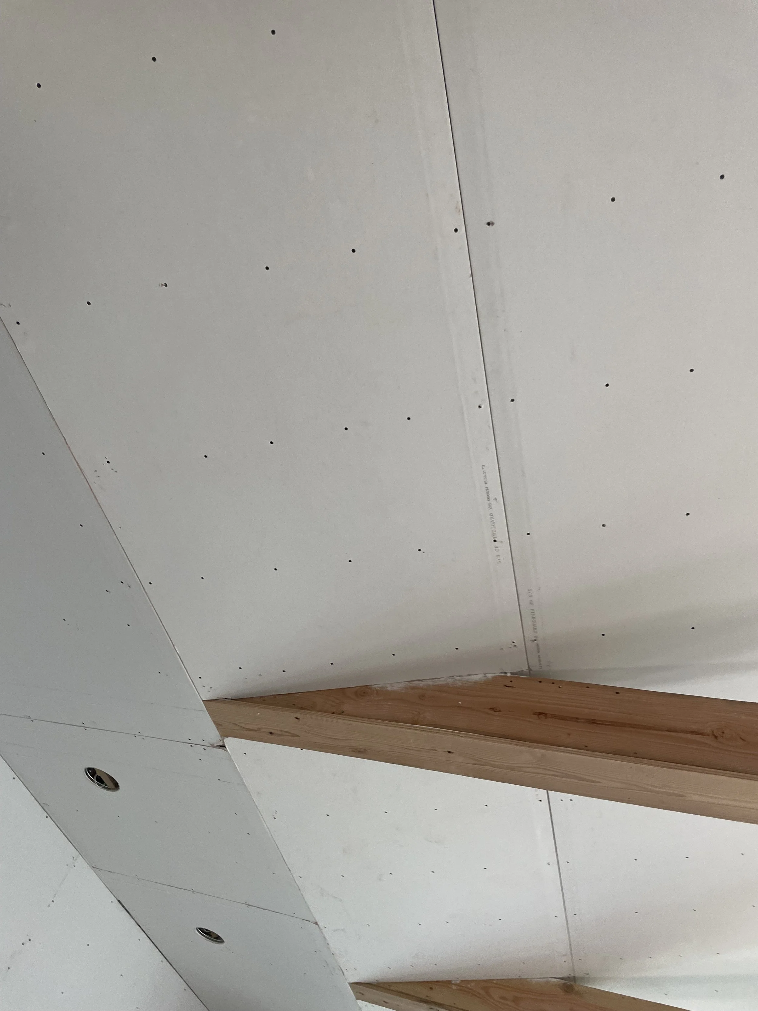 Partially finished ceiling with drywall and wooden beams.