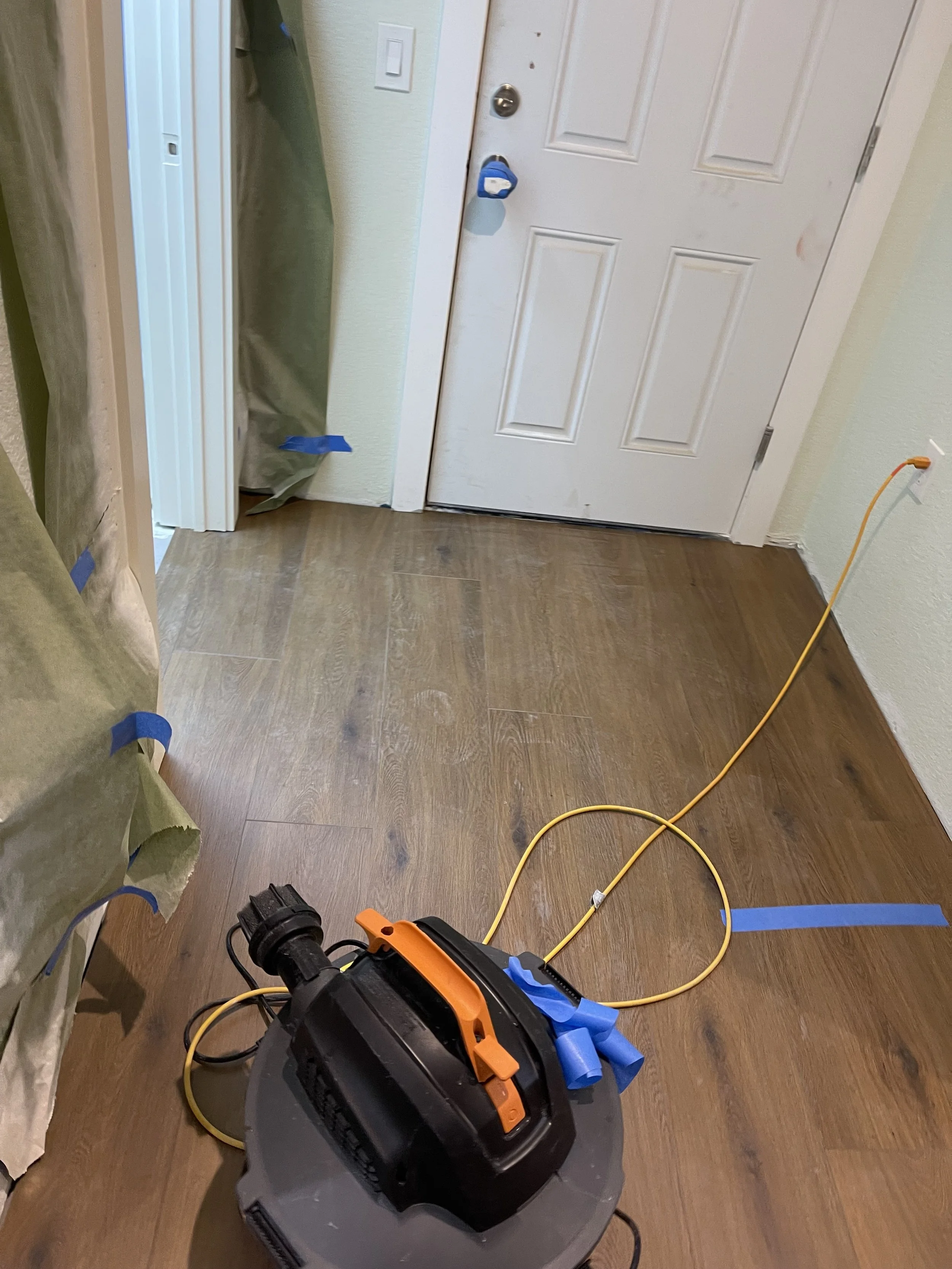 Entryway with a new hardwood floor, a white door, and a power tool with yellow extension cord on the floor.