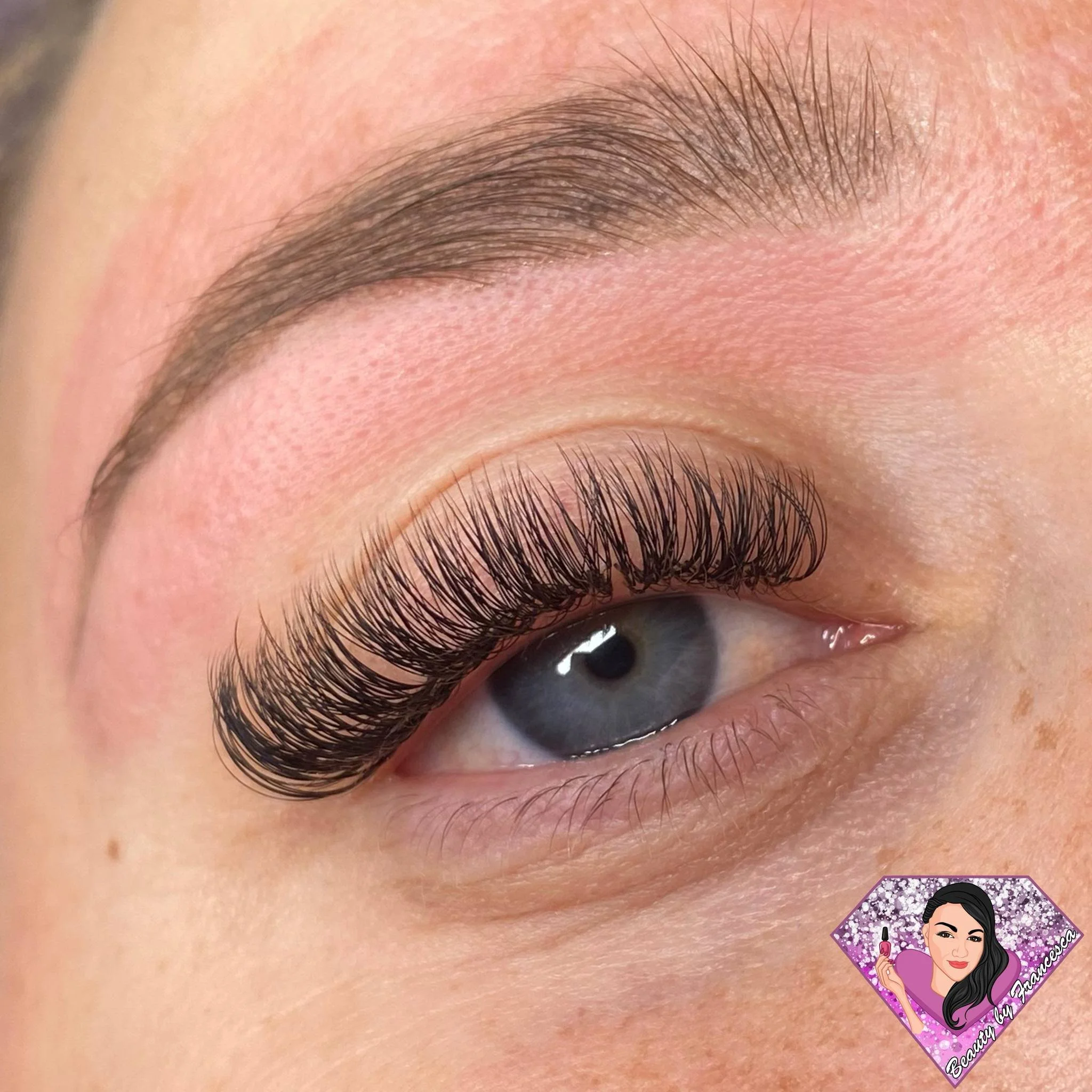 Close-up of a person's eye with long, curled eyelashes, blue iris, and well-groomed eyebrow.