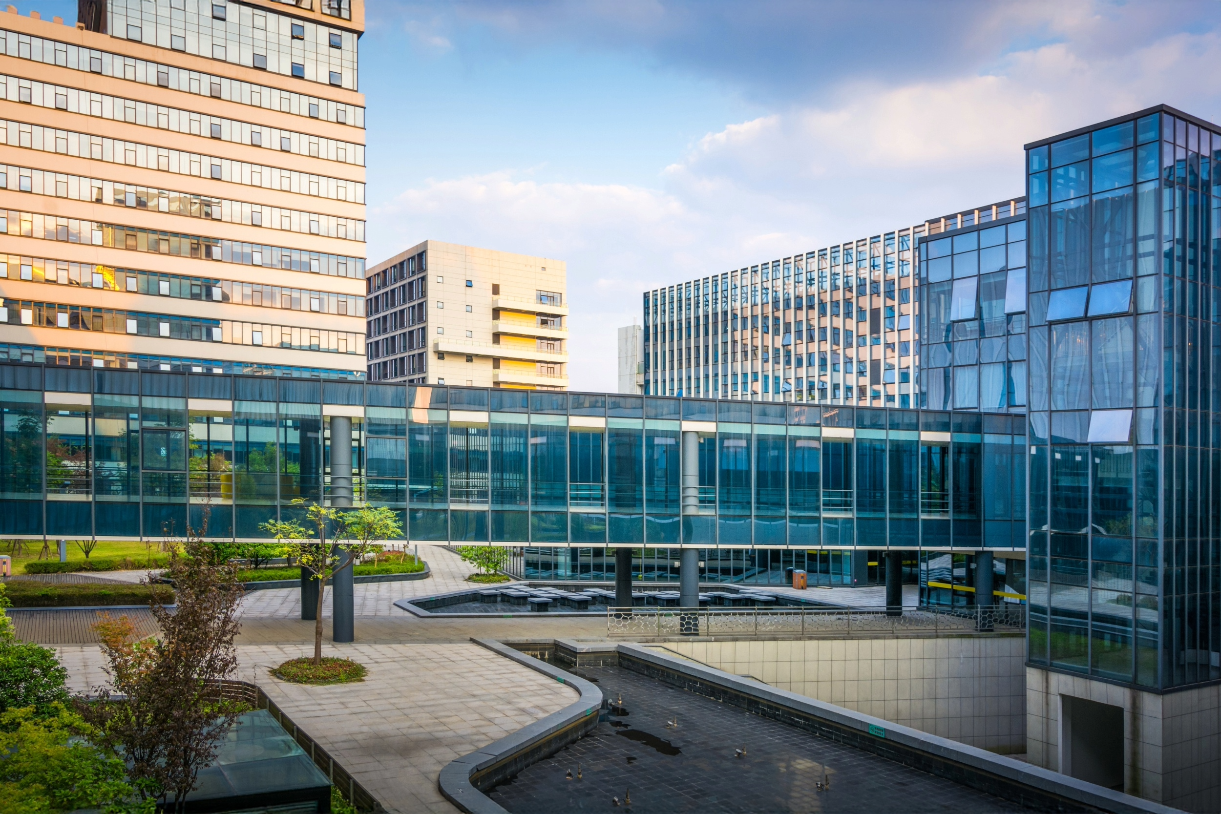 Modern cityscape with tall office buildings and a glass connecting bridge in an urban environment during daytime.