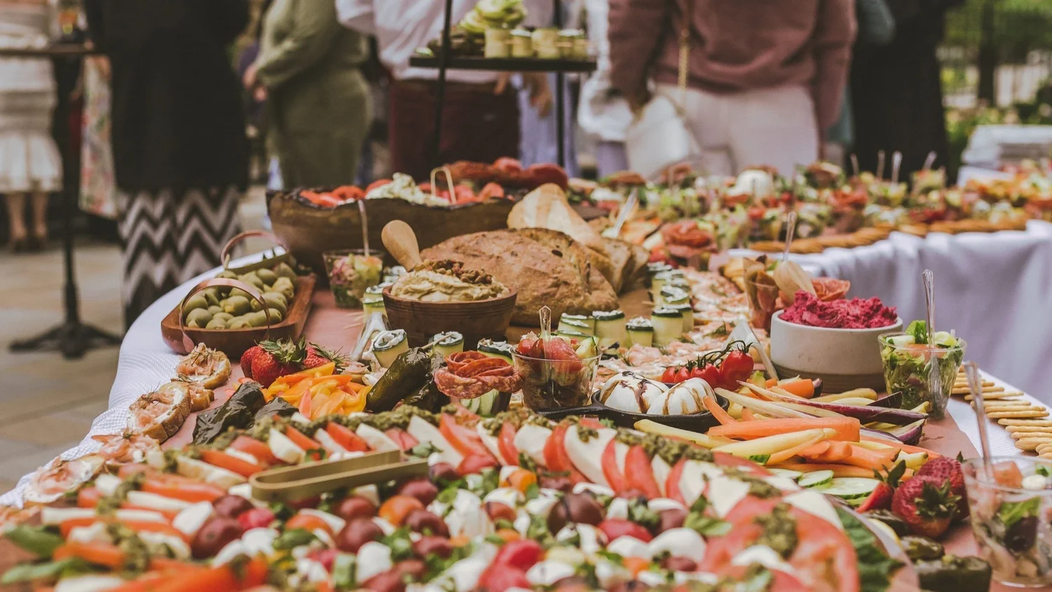 An abundant outdoor grazing table with cheeses, vegetables, breads and dips