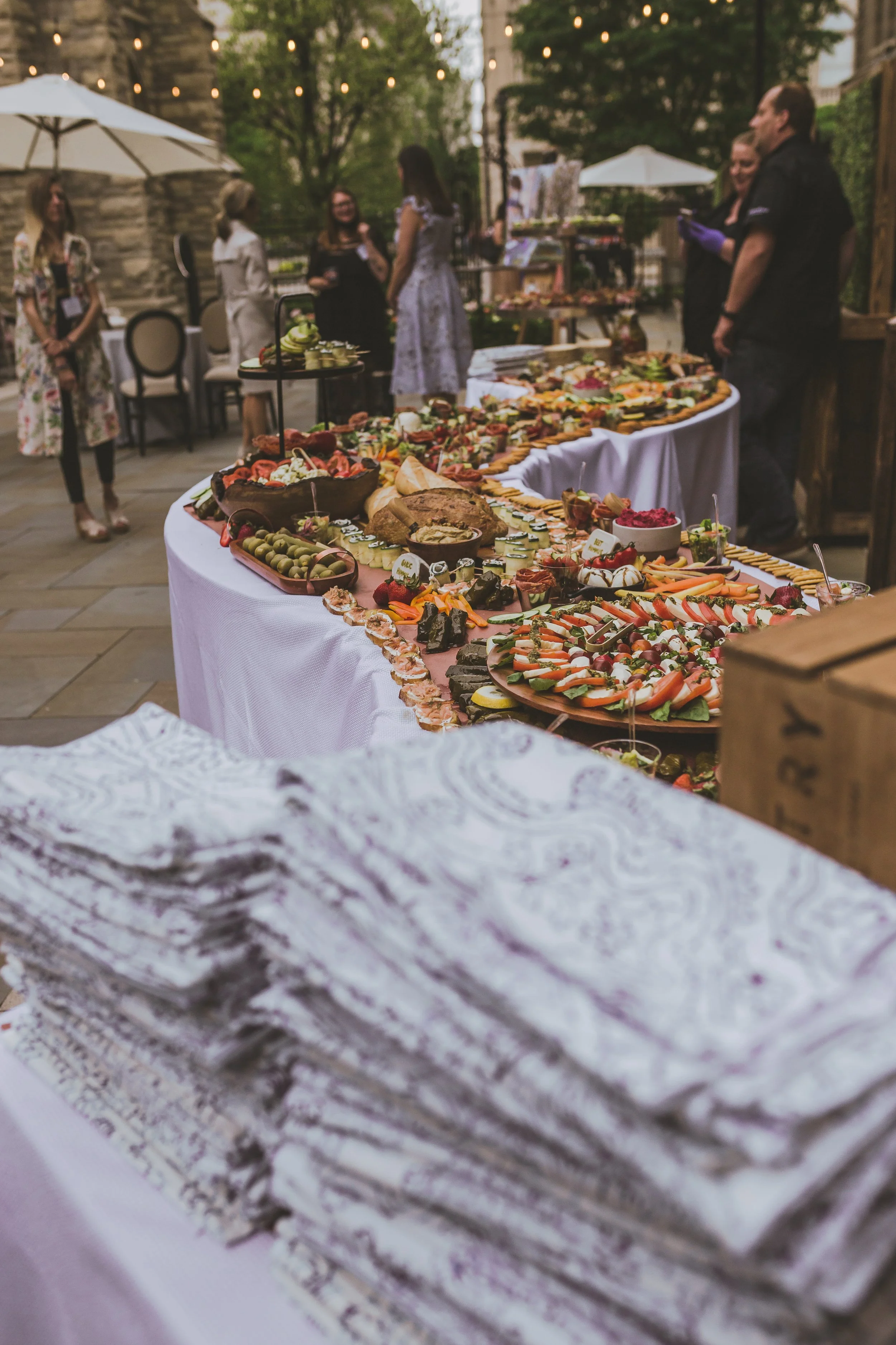 Outdoor buffet table with a variety of appetizers at a social gathering, with people in the background.