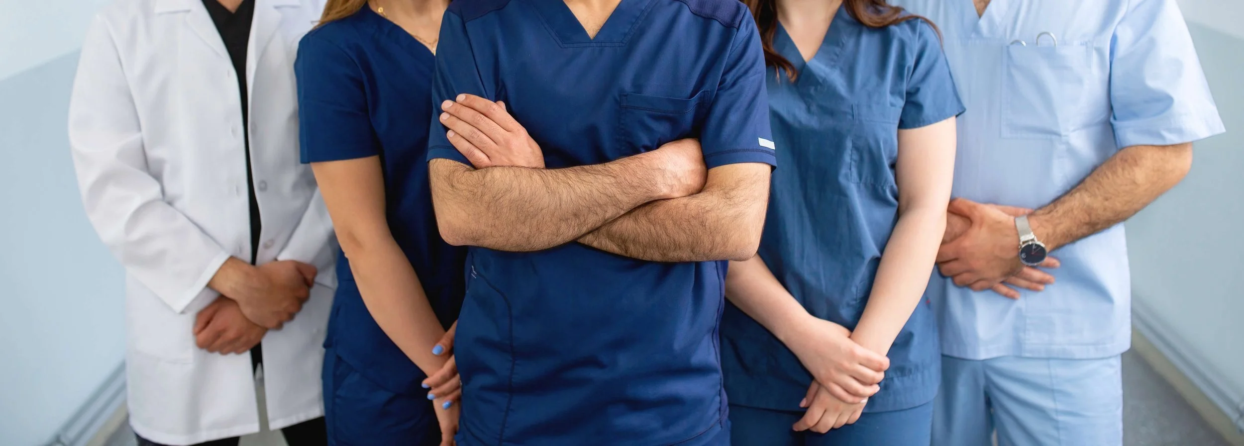 Group of medical professionals wearing scrubs and lab coats standing together in a hospital corridor.