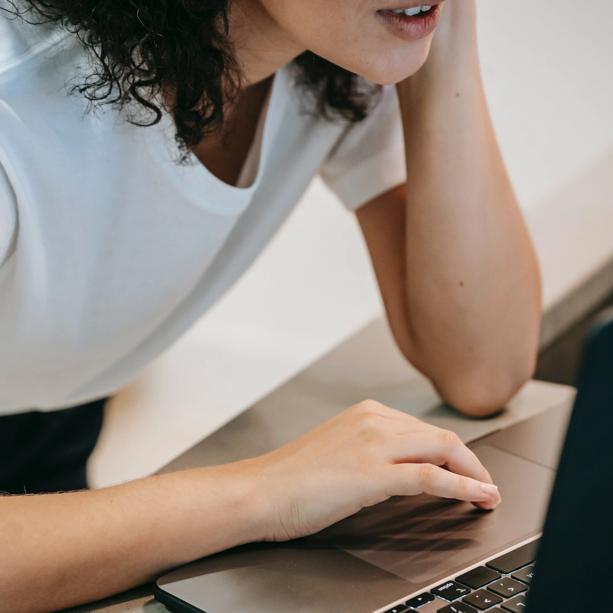 A woman with curly hair working on a laptop, resting her chin on her hand.
