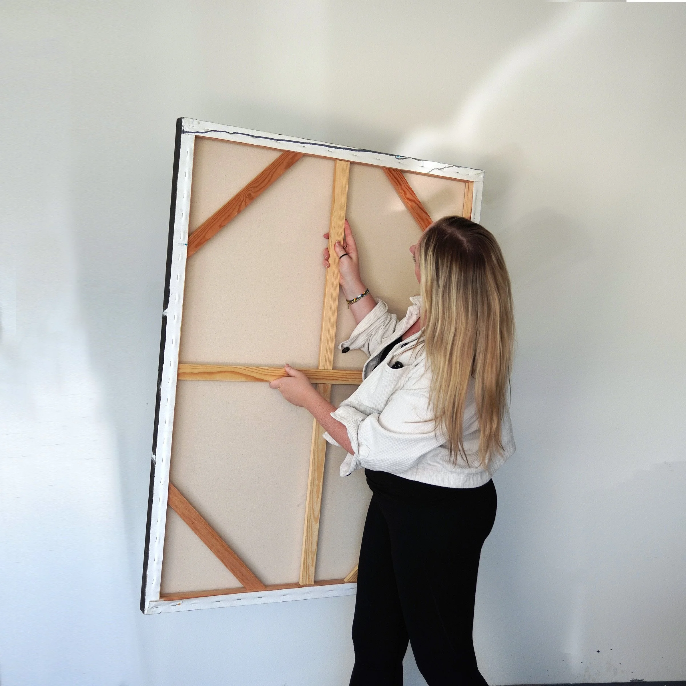 artist liz lancaster holding a large canvas in a white art studio