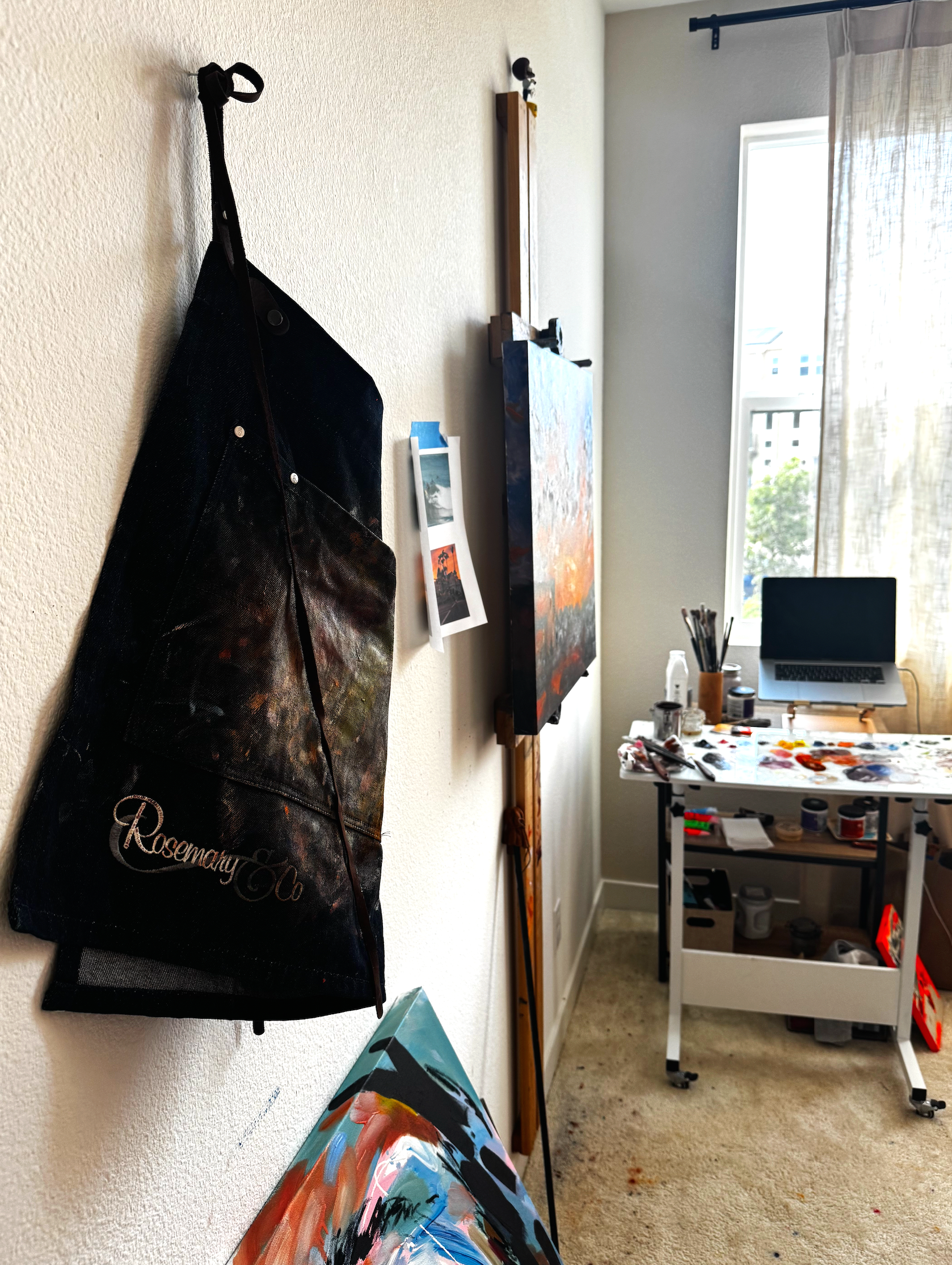 detail shot of an artists studio with a paint covered rosemary denim apron and an easel and palette in the background