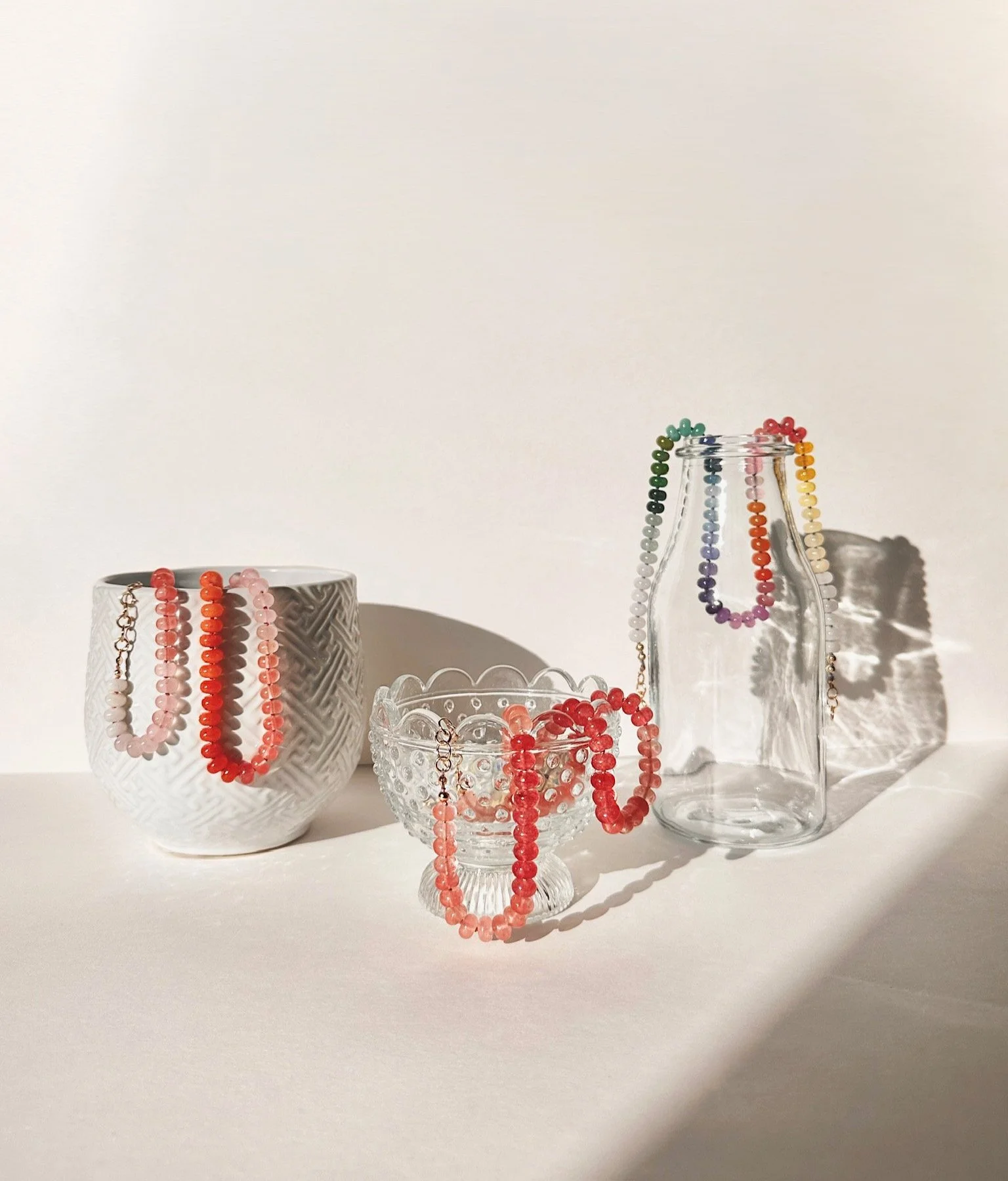Colorful beaded necklaces draped over glass containers on a white surface with a plain white background.