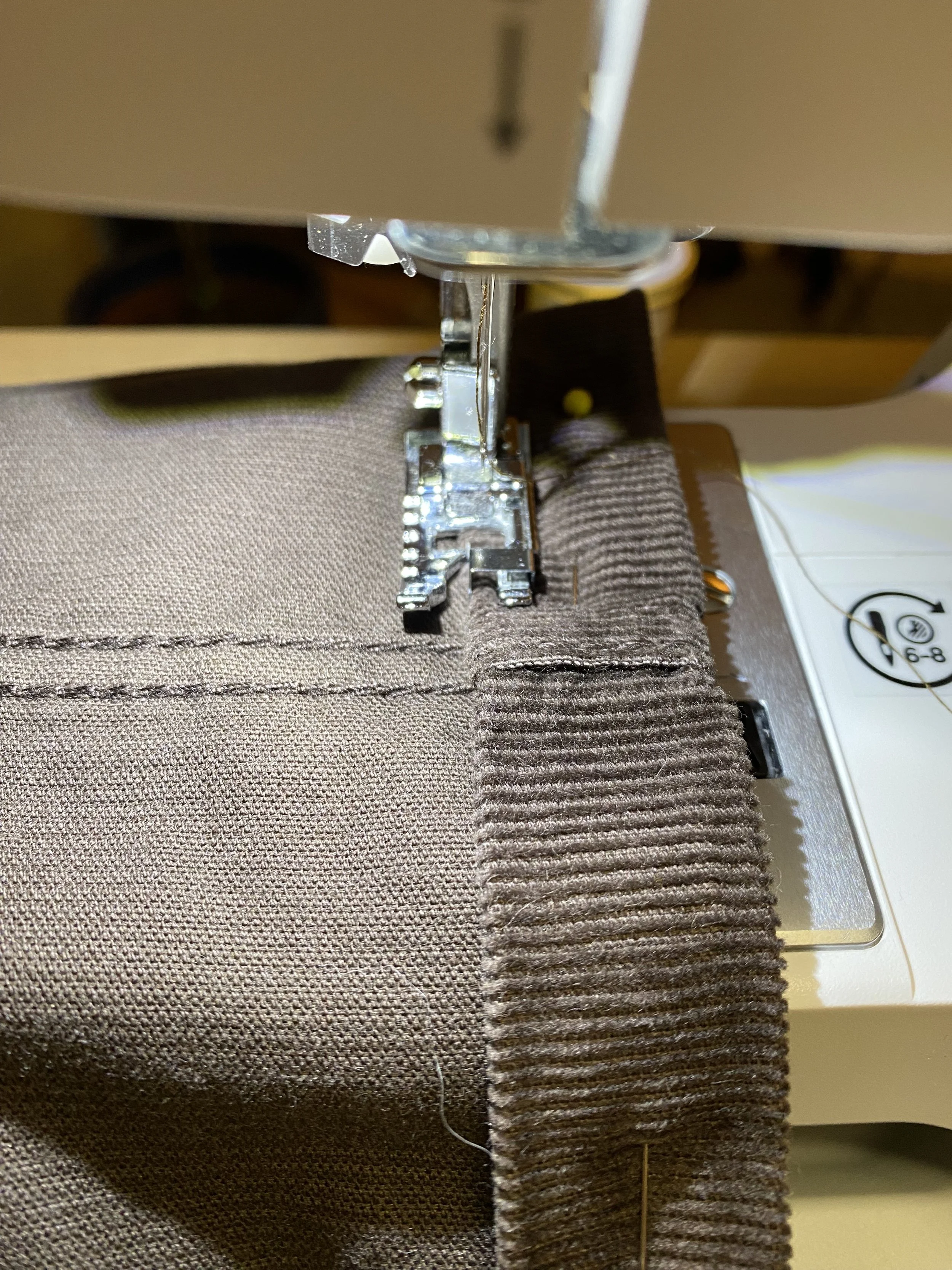 Close-up of a sewing machine stitching a brown fabric with a stitched seam and ruffled edge.