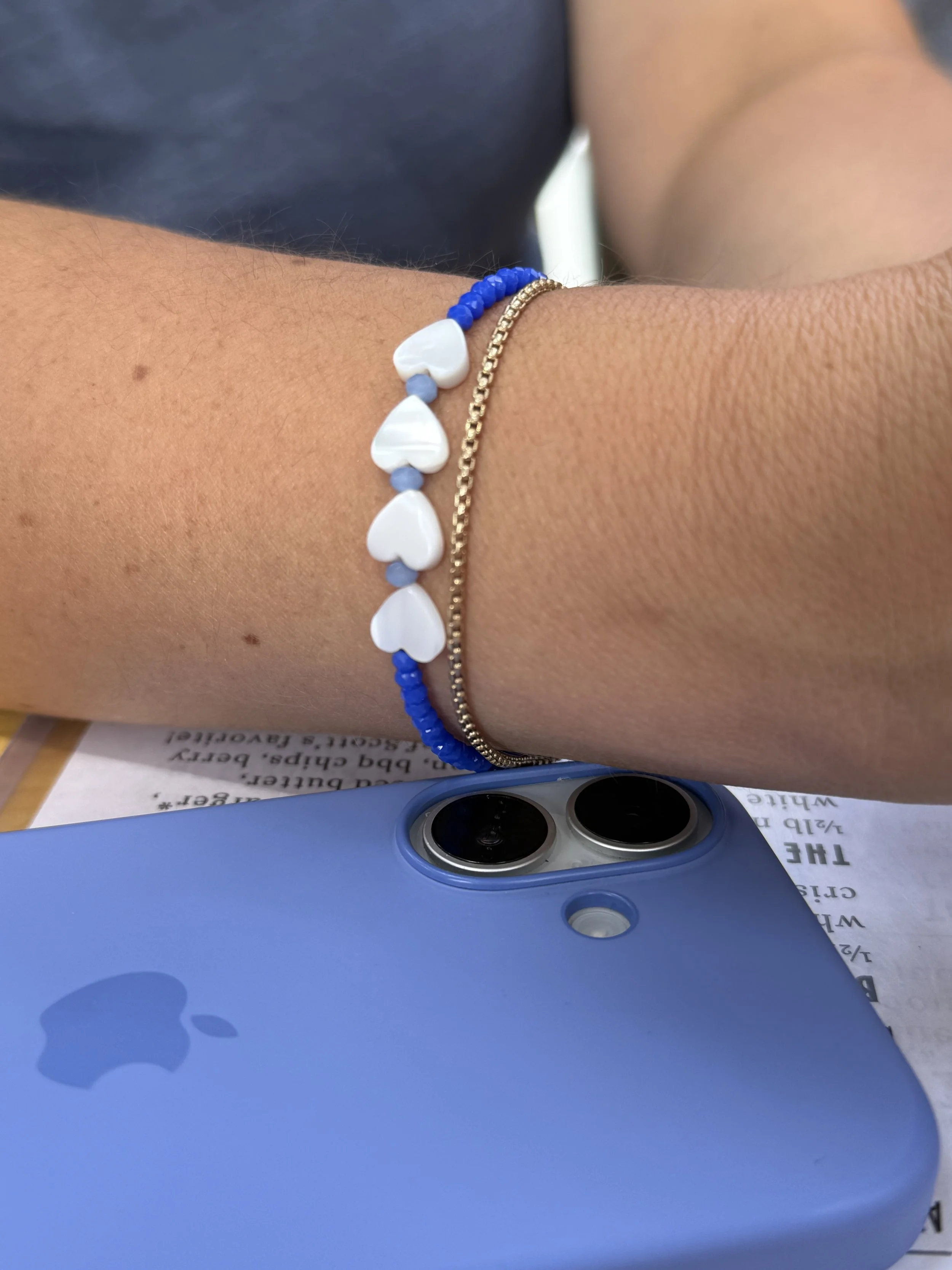 Close-up of a person's wrist wearing three bracelets, with a blue iPhone with dual camera lenses in the background.