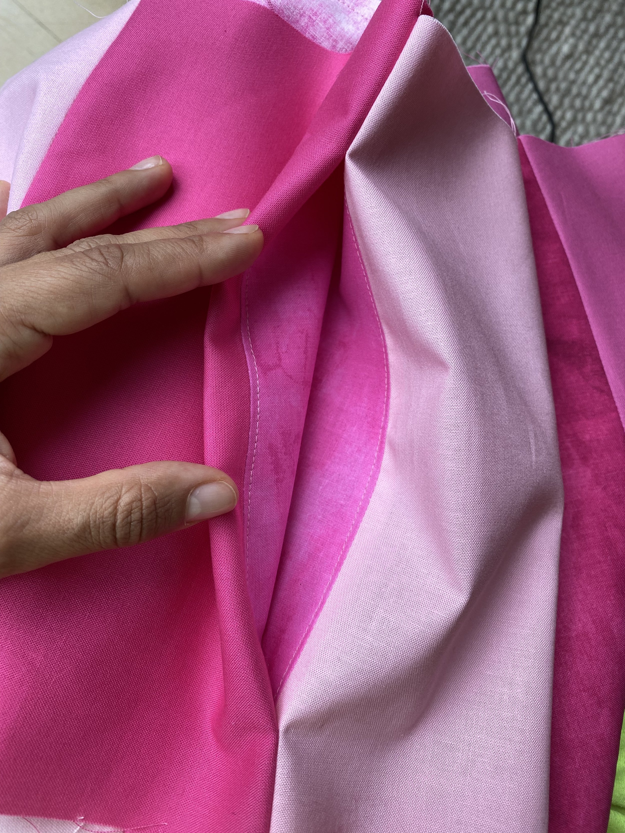 Close-up of a hand holding pink and light pink fabric with different textures and shades.