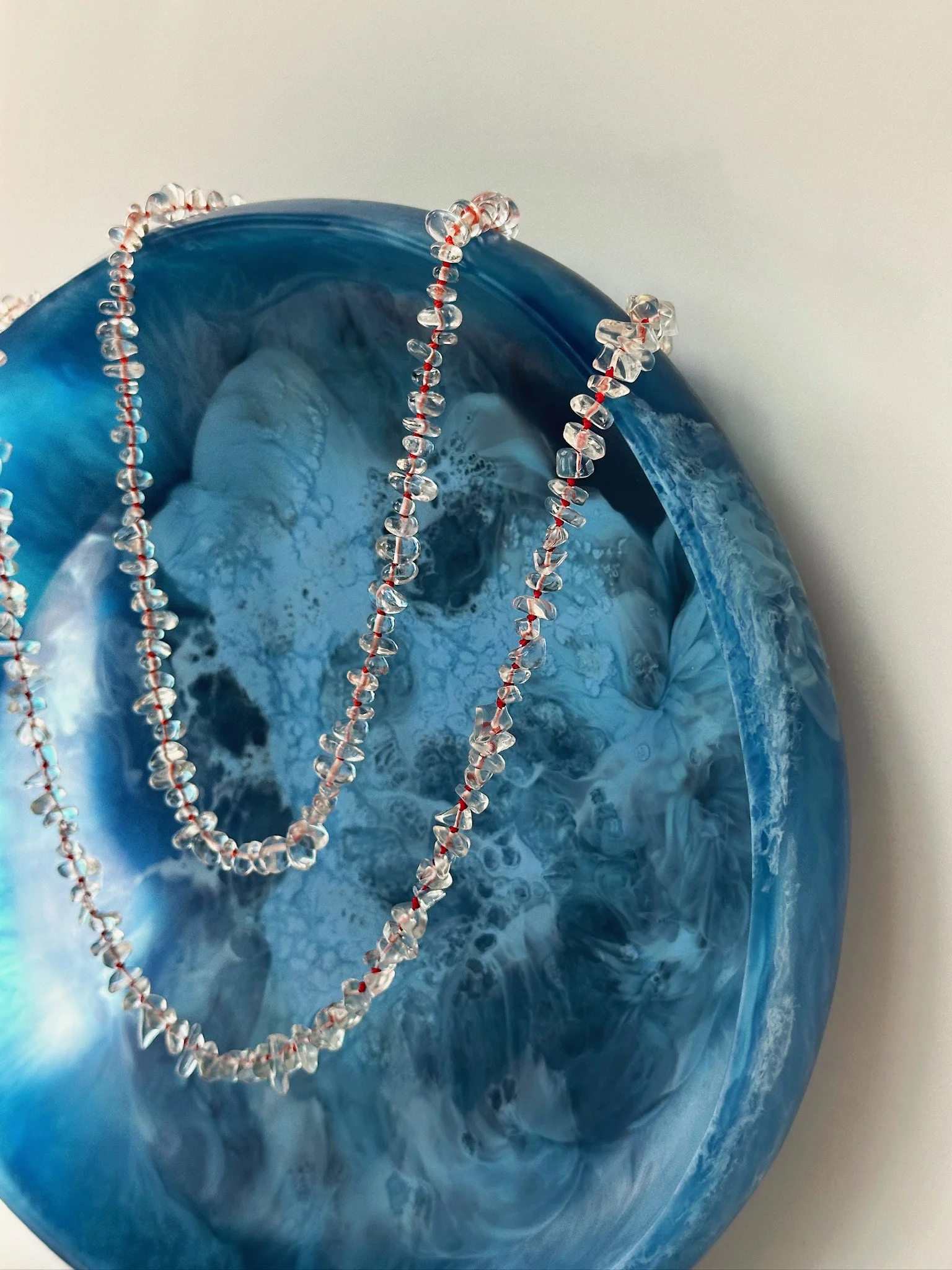 A blue and white marbled glass vase with a clear beaded necklace draped over it.