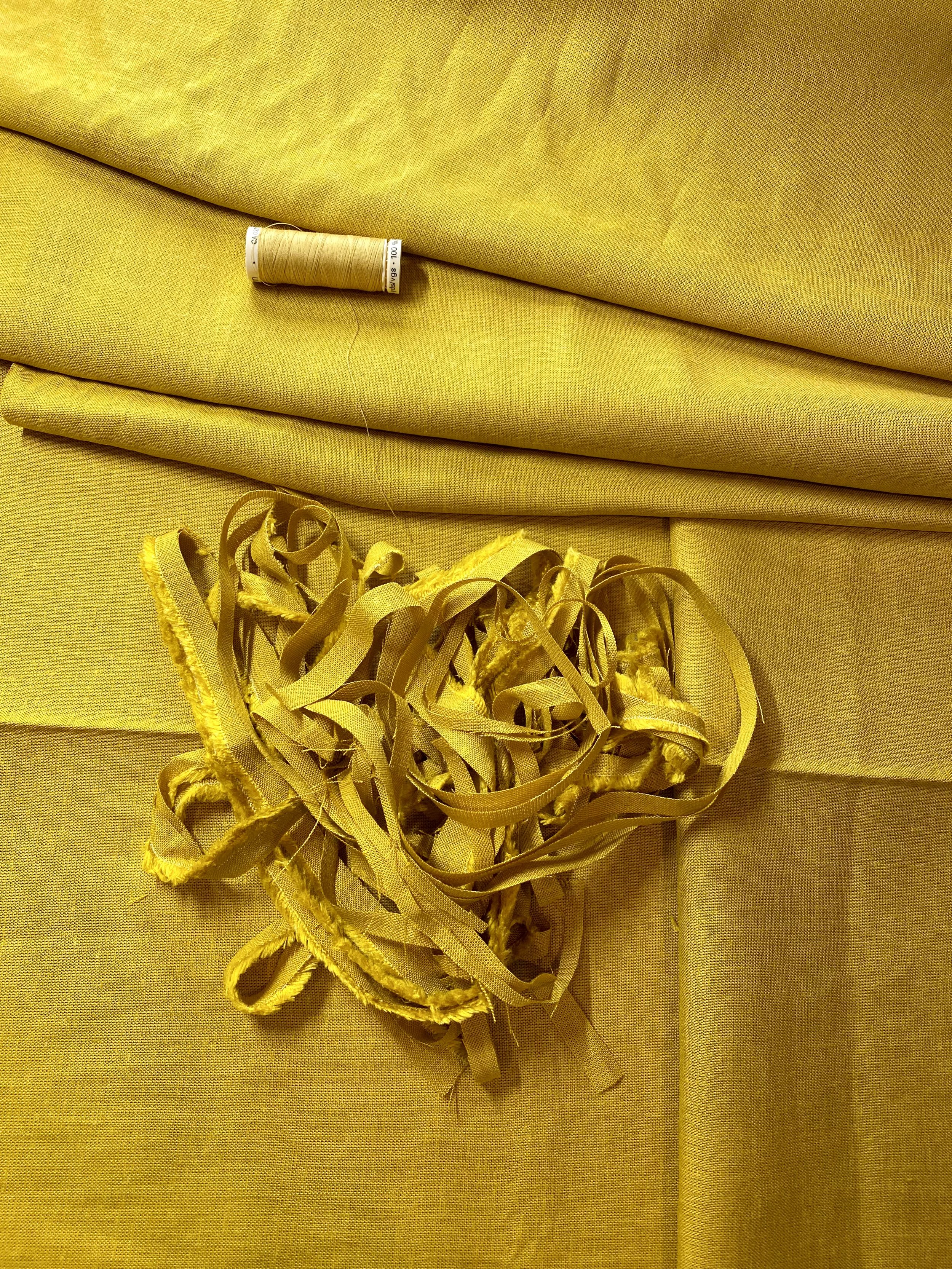 Yellow fabric with a thread spool on top and a pile of yellow fabric scraps below.