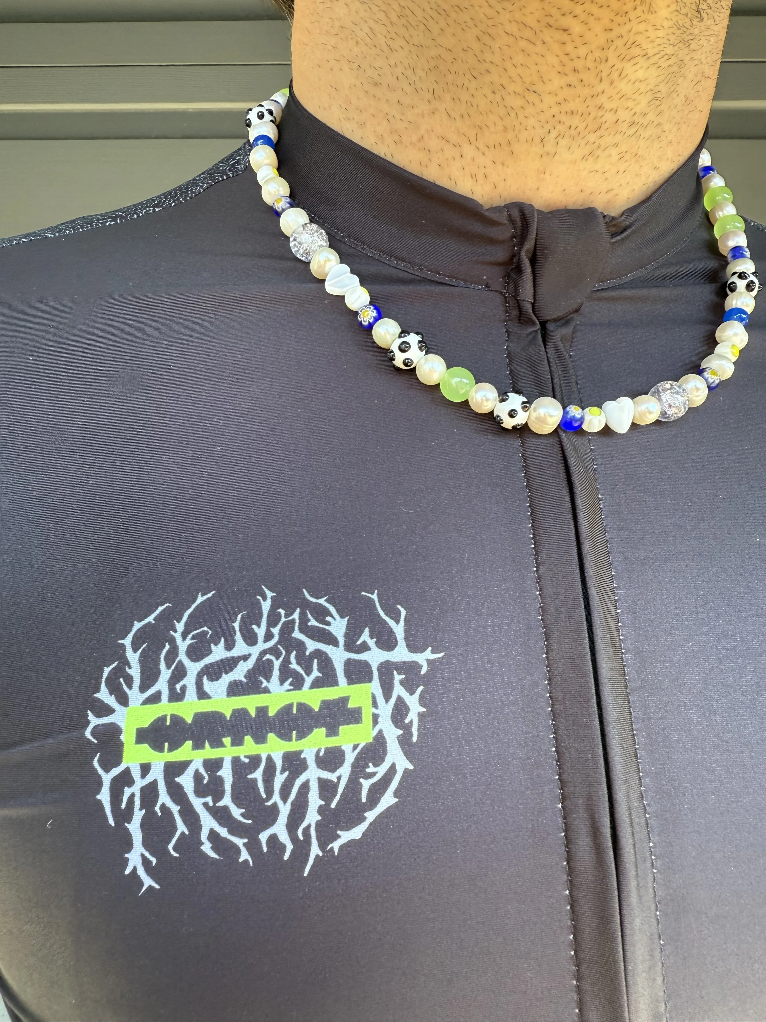 Person wearing a black athletic jacket with a graphic and a yellow highlight reading 'SOUND' and a beaded necklace with panda, heart, and colorful beads.