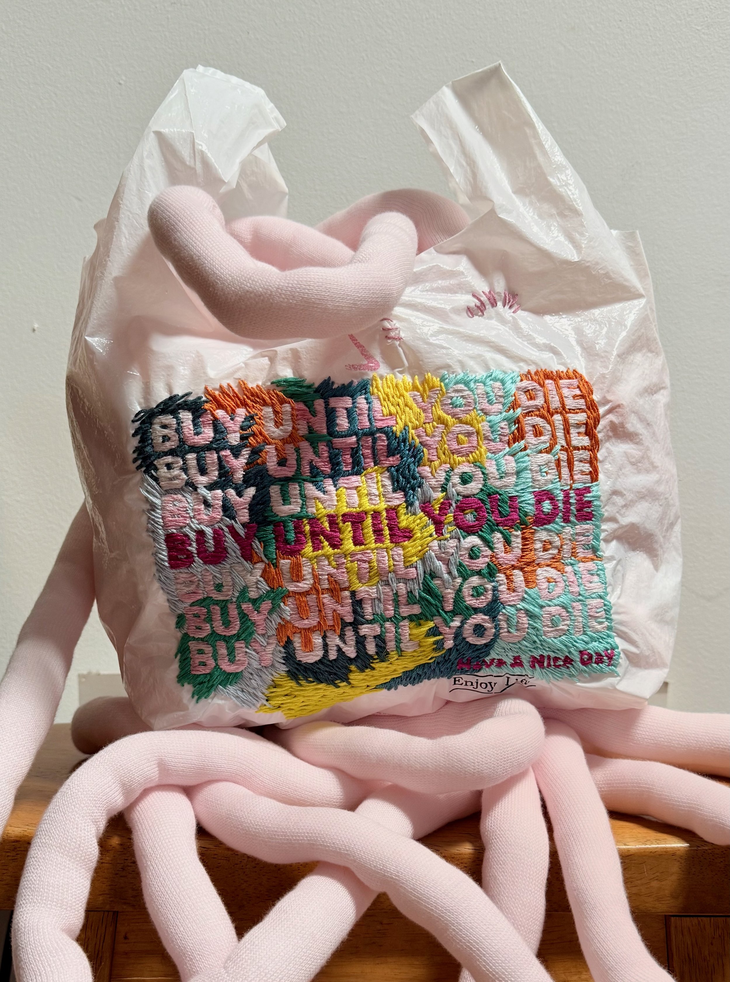 BUY UNTIL YOU DIE, 2026. Hand embroidery on plastic bag, plush yarn.