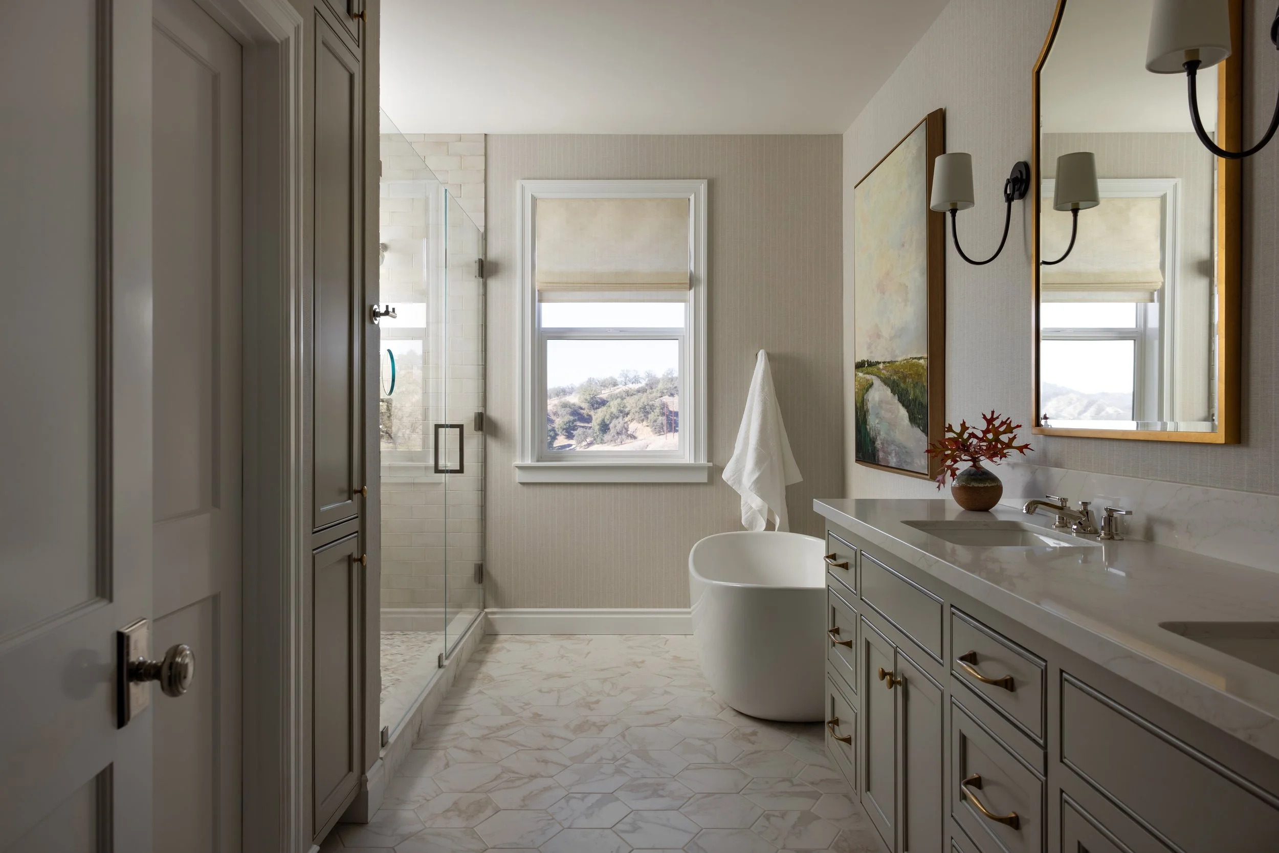 Primary bathroom with freestanding soaking tub, mosaic tile floor, glass shower, gray double vanity, and hillside views — Bartlett Residence by Tama Bell Design, Ukiah CA